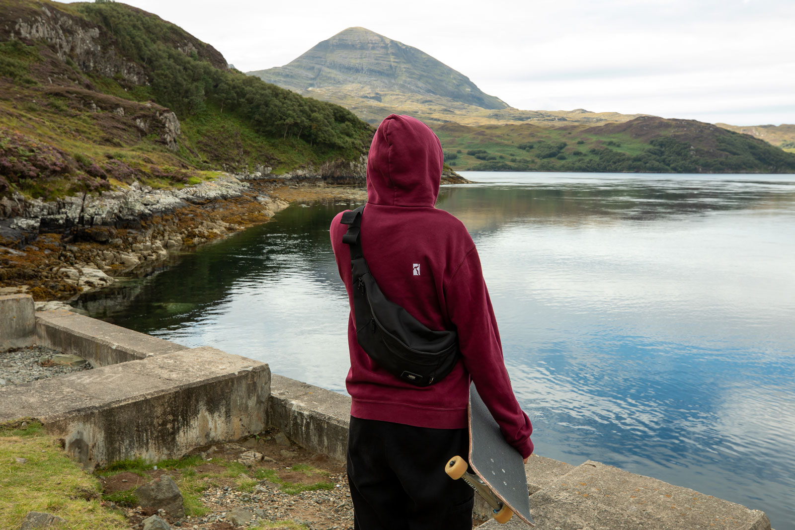 Skateboarder wearing a red hoodie staring out at a lake