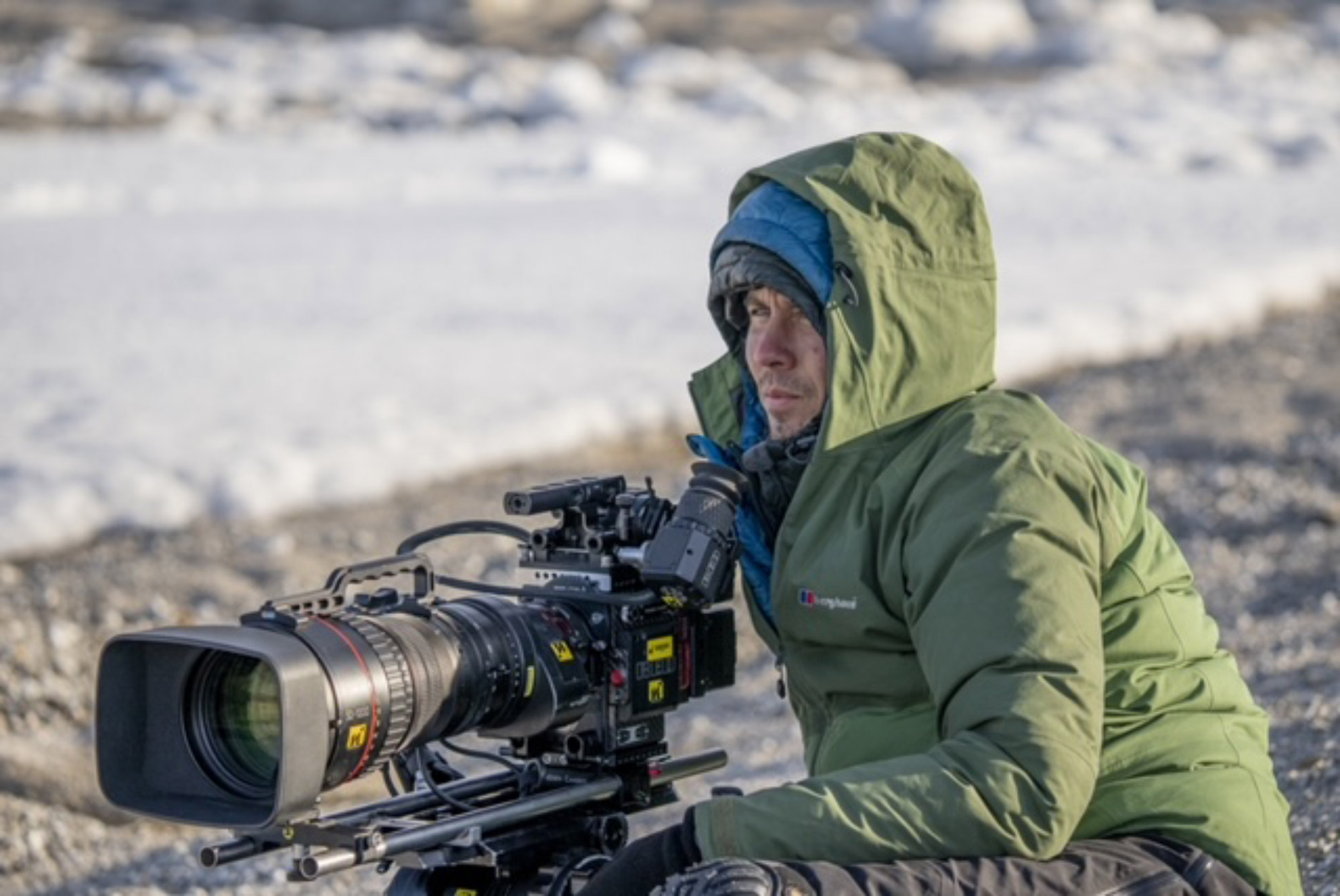 Alex Vail sitzt auf dem Boden und hält eine Kamera in der Hand, im Hintergrund liegt Schnee