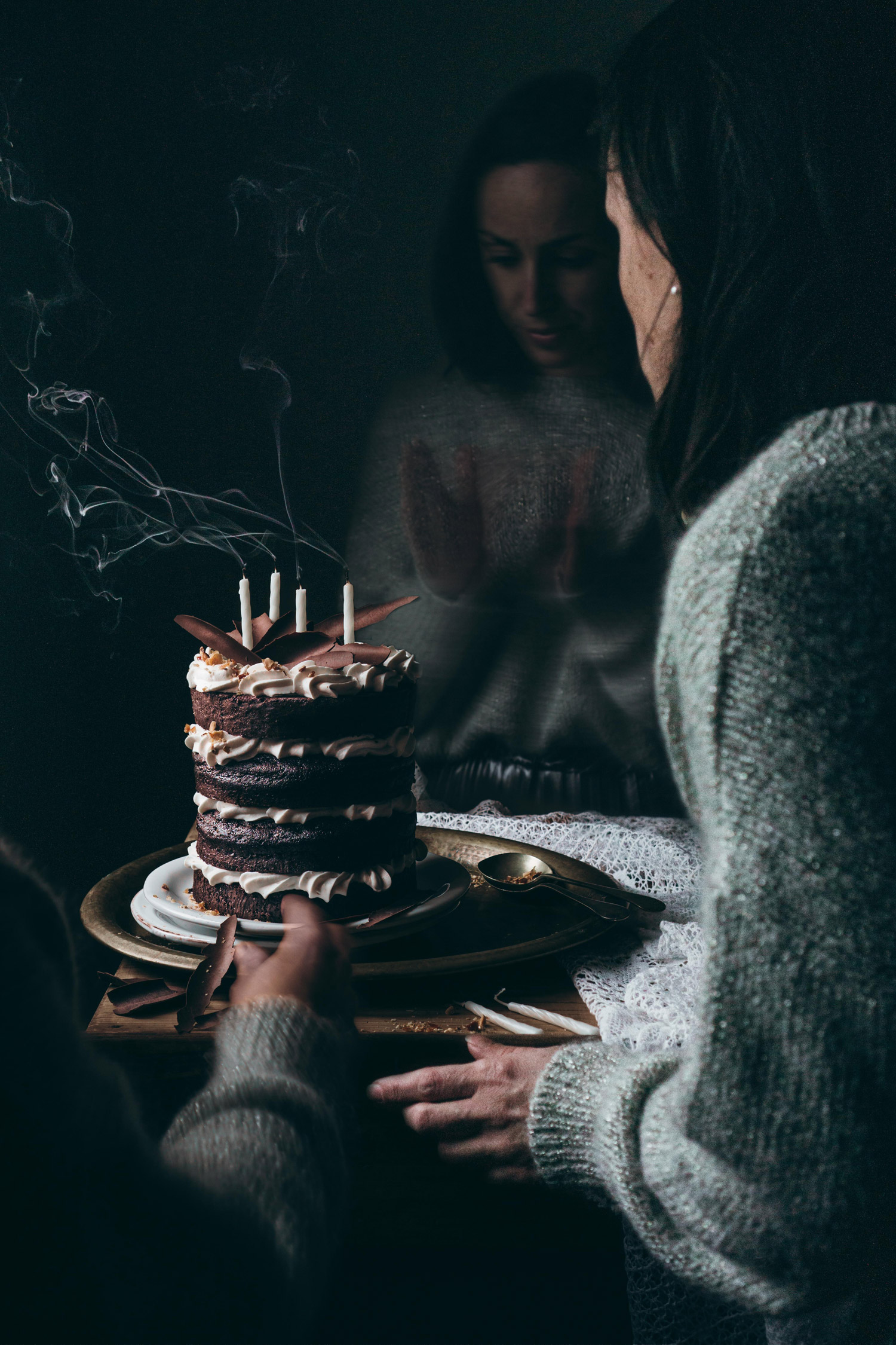 Elisa De Cecchi looks at a multi-layered chocolate birthday cake, with smoke coming from four candles on the top.