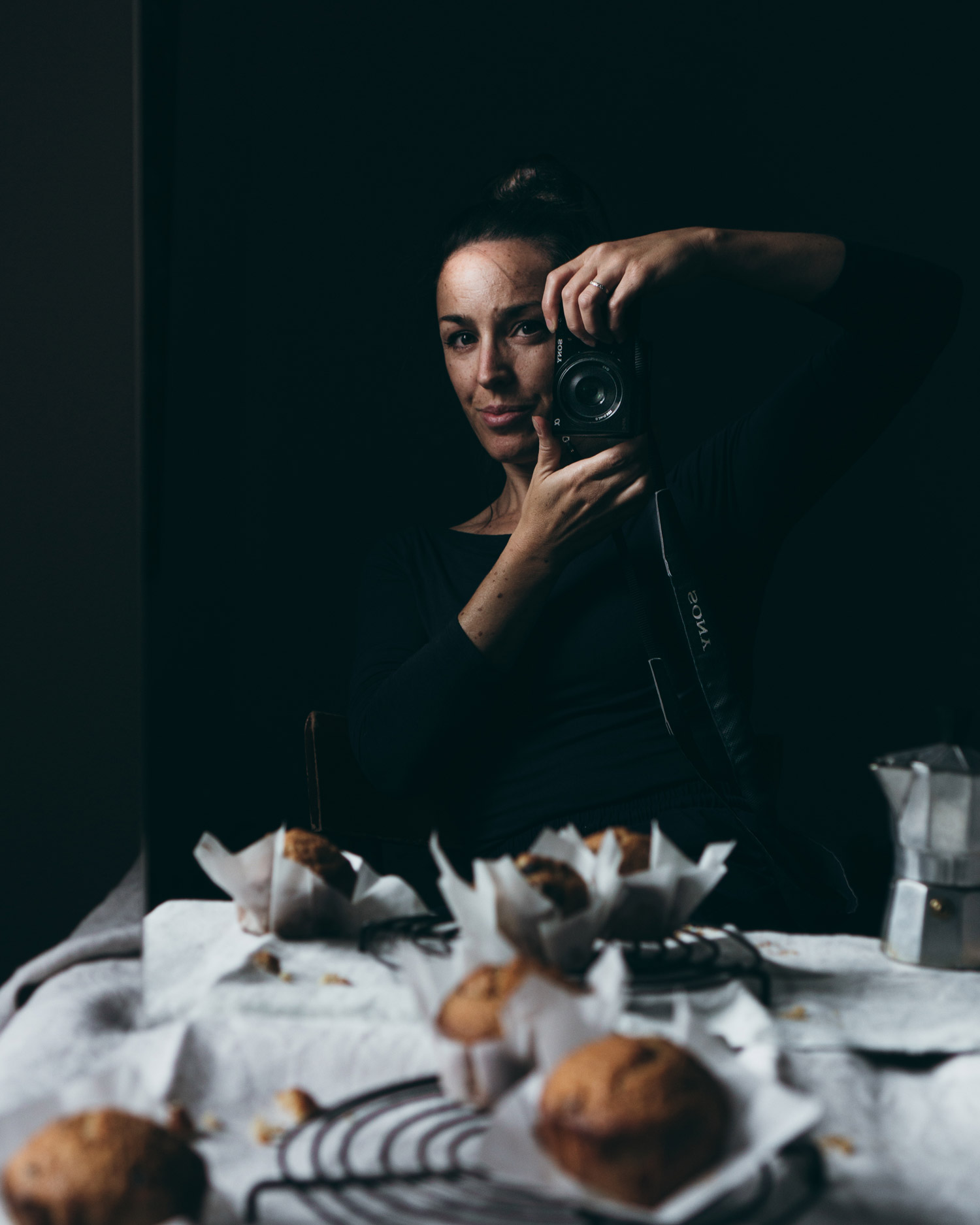 Elisa De Cecchi hält eine Kamera in der Hand, hinter einem Tisch mit Muffins und einem Wasserkocher.