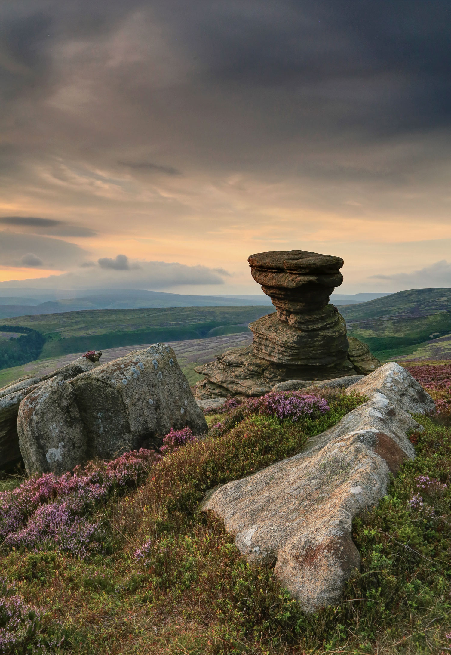 Two large boulders and a stack of smaller stones on the floor with hills and valleys in the background.