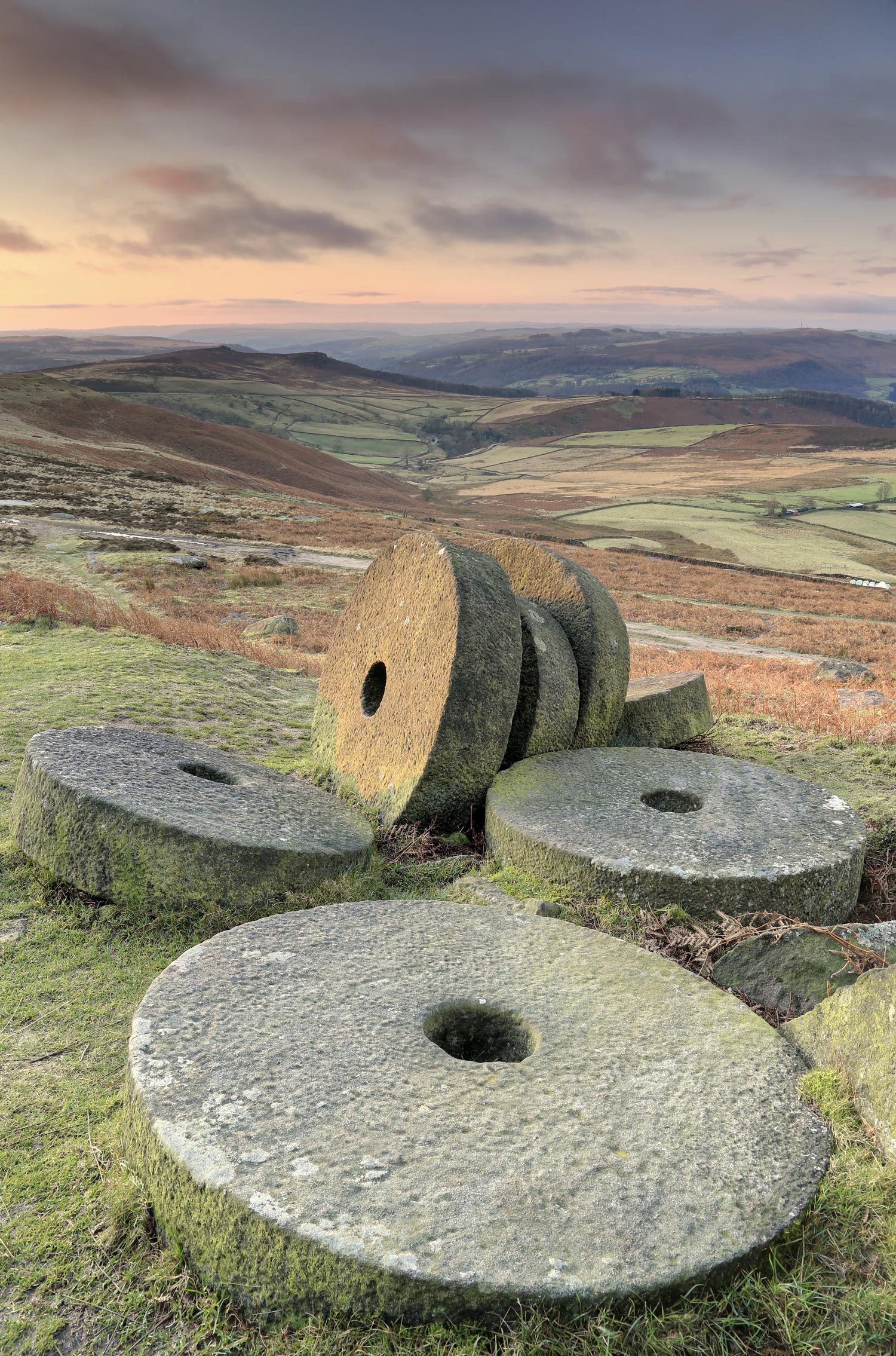 Circular stones with holes in the middle on the floor with hills and valleys in the background.
