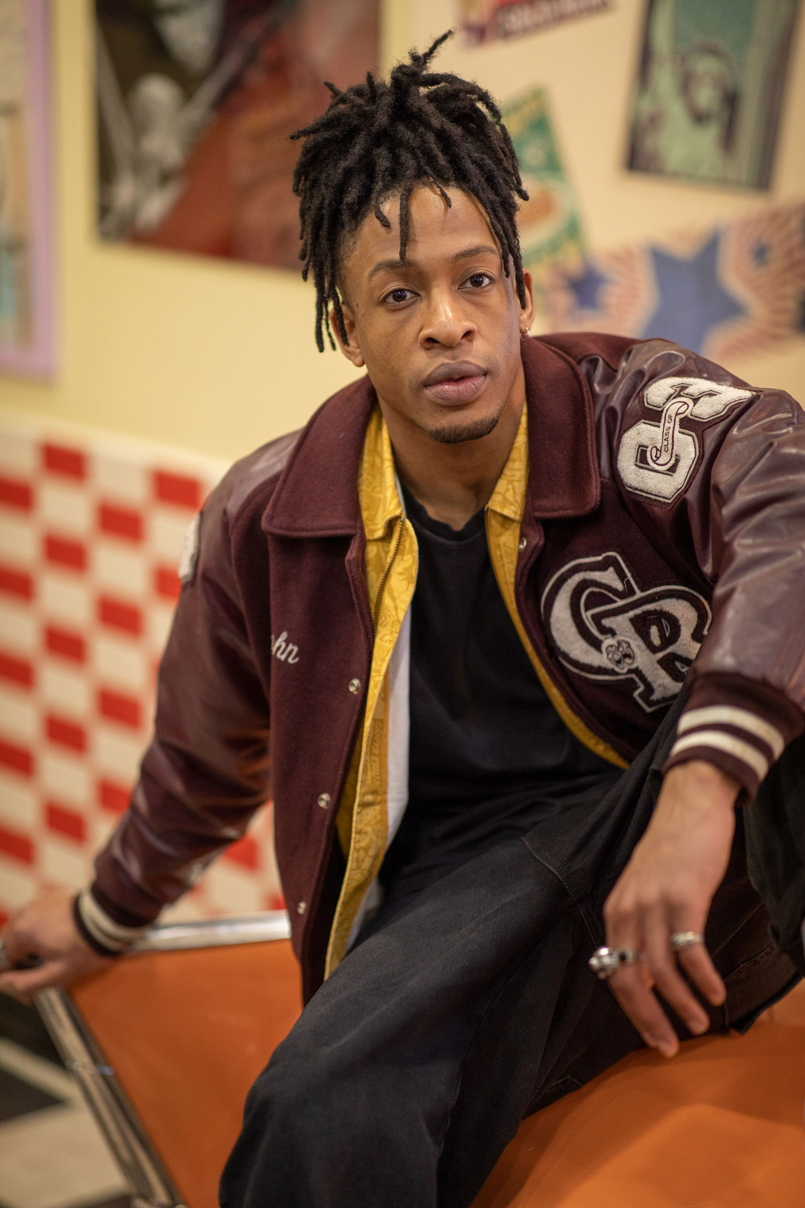 A model wearing a brown sports jacket sits on an orange couch. Shot with Canon EOS 5D Mark IV + Canon 85mm f/1.4 L IS.