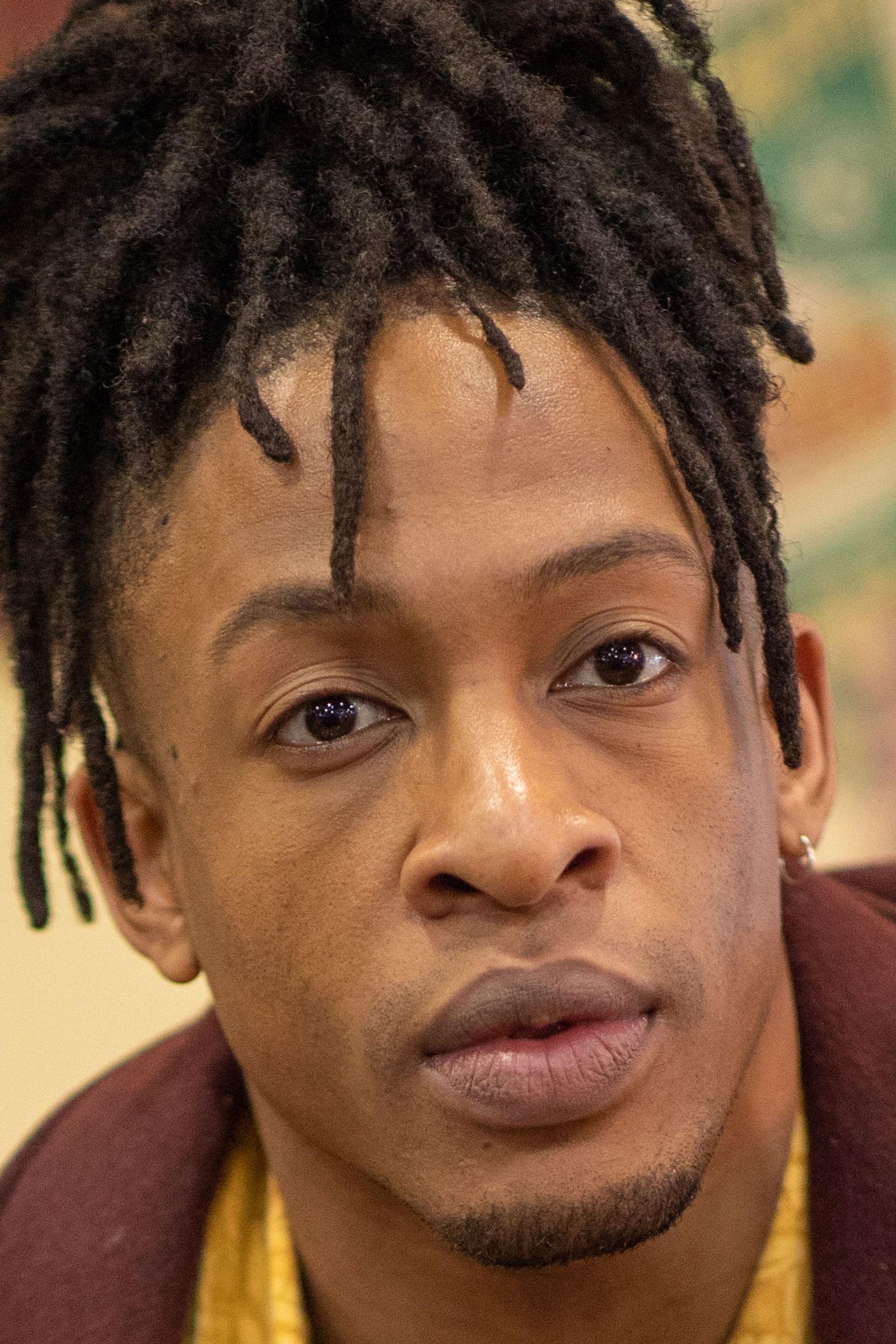 100% crop to demonstrate sharpness and rendering of Canon EF 85mm f/1.4 L IS. A model wearing a brown sports jacket sits on an orange couch. Shot with Canon EOS 5D Mark IV + Canon 85mm f/1.4 L IS.