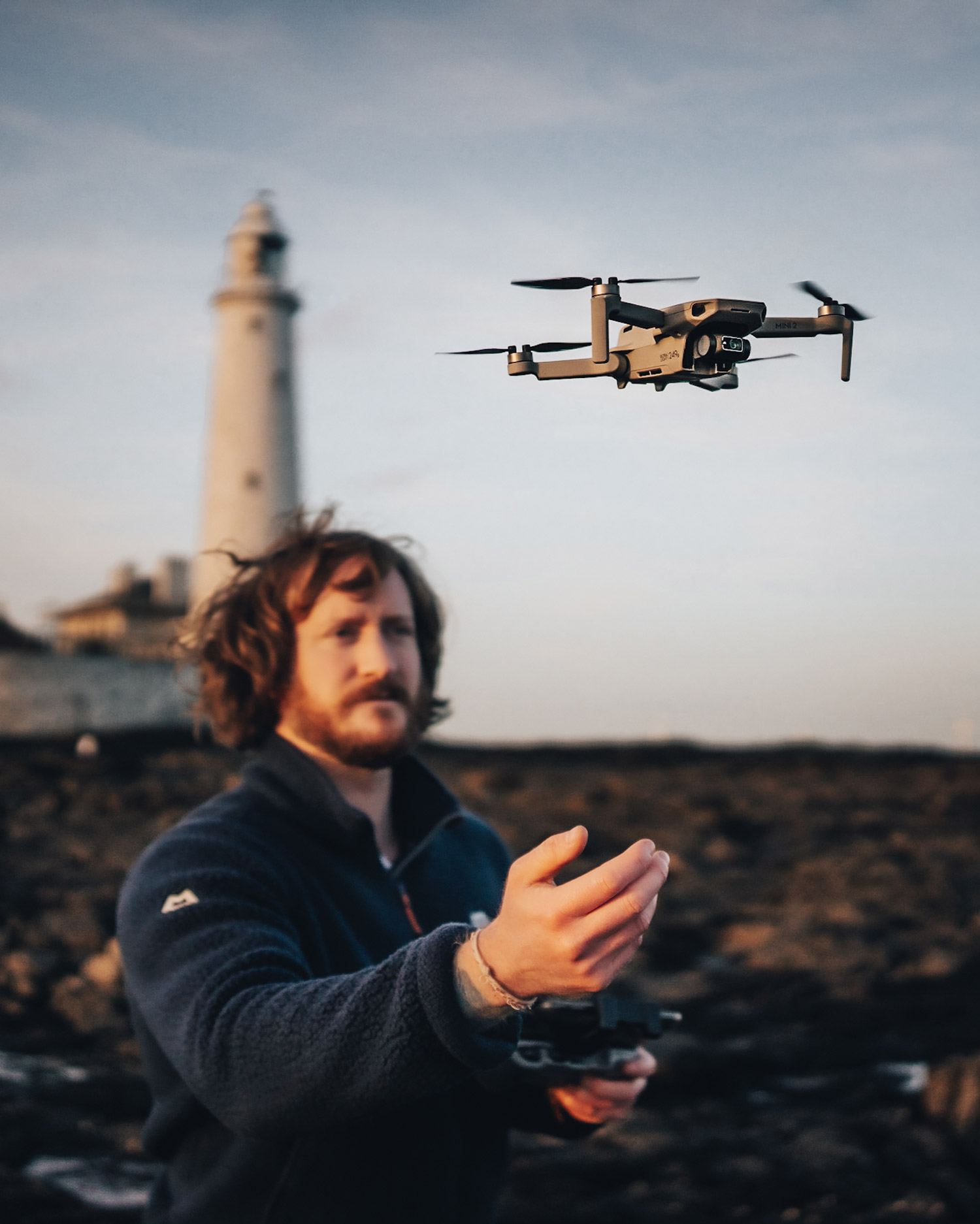 Adam Parkinson lève la main vers un DJI Mini 2 en vol avec un phare en arrière-plan.