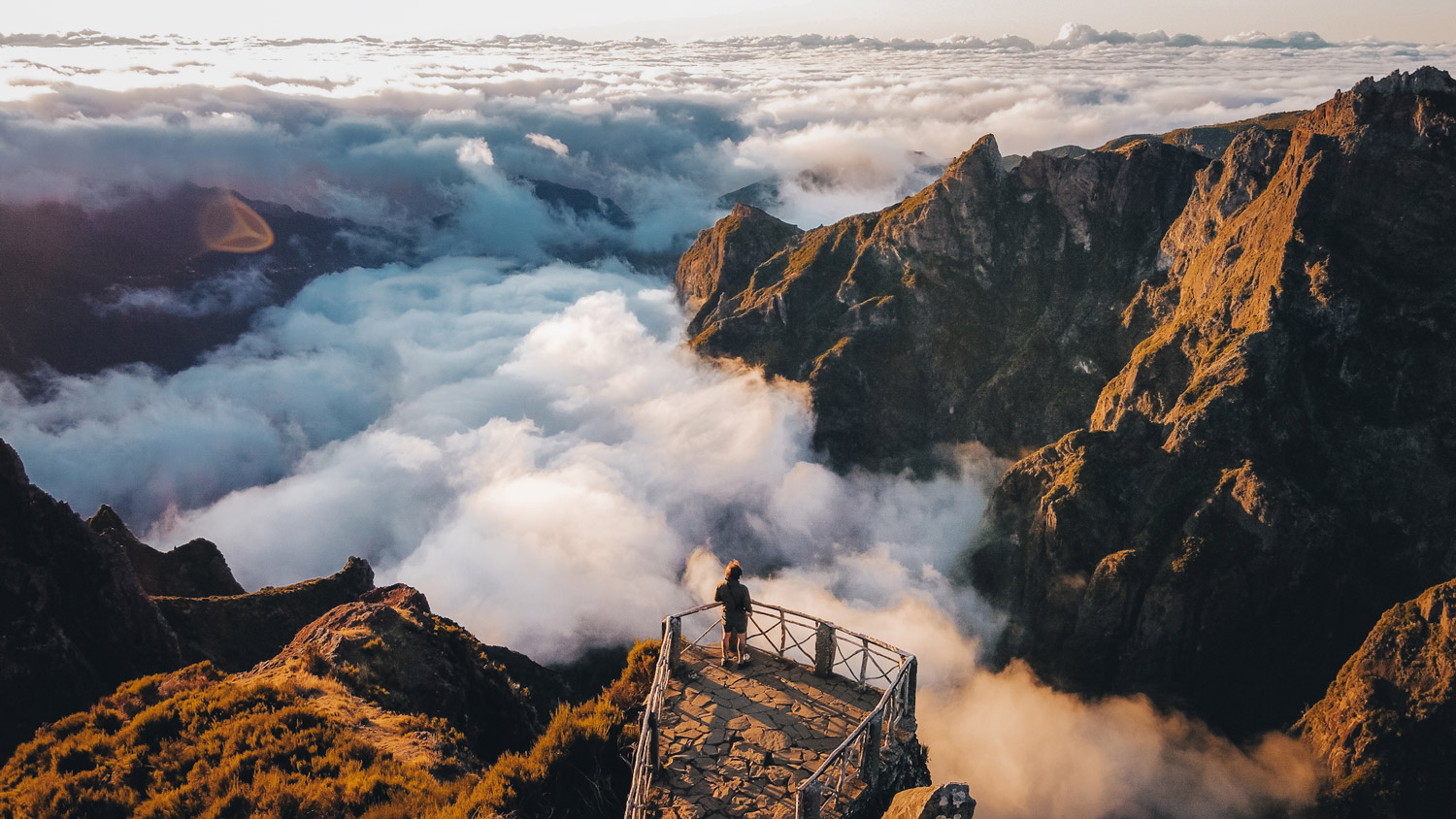 Une chaîne de montagnes avec des nuages roulant au sommet. Une personne se tient sur une plate-forme d'observation.