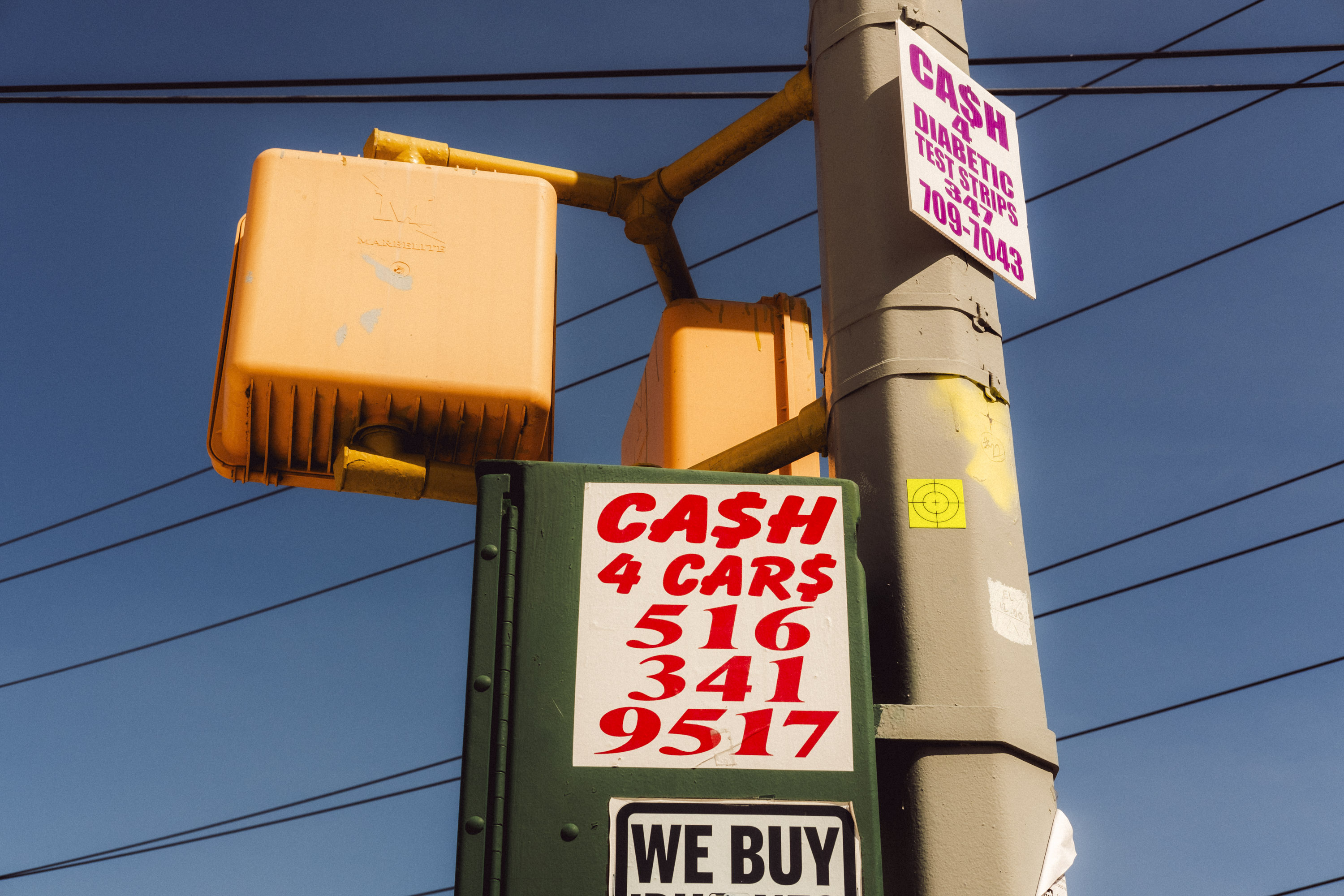 A low-angle image of a street lamp pole with various signs and traffic lights attached to it. Shot on the X-Pro 3 by Ian Howorth.