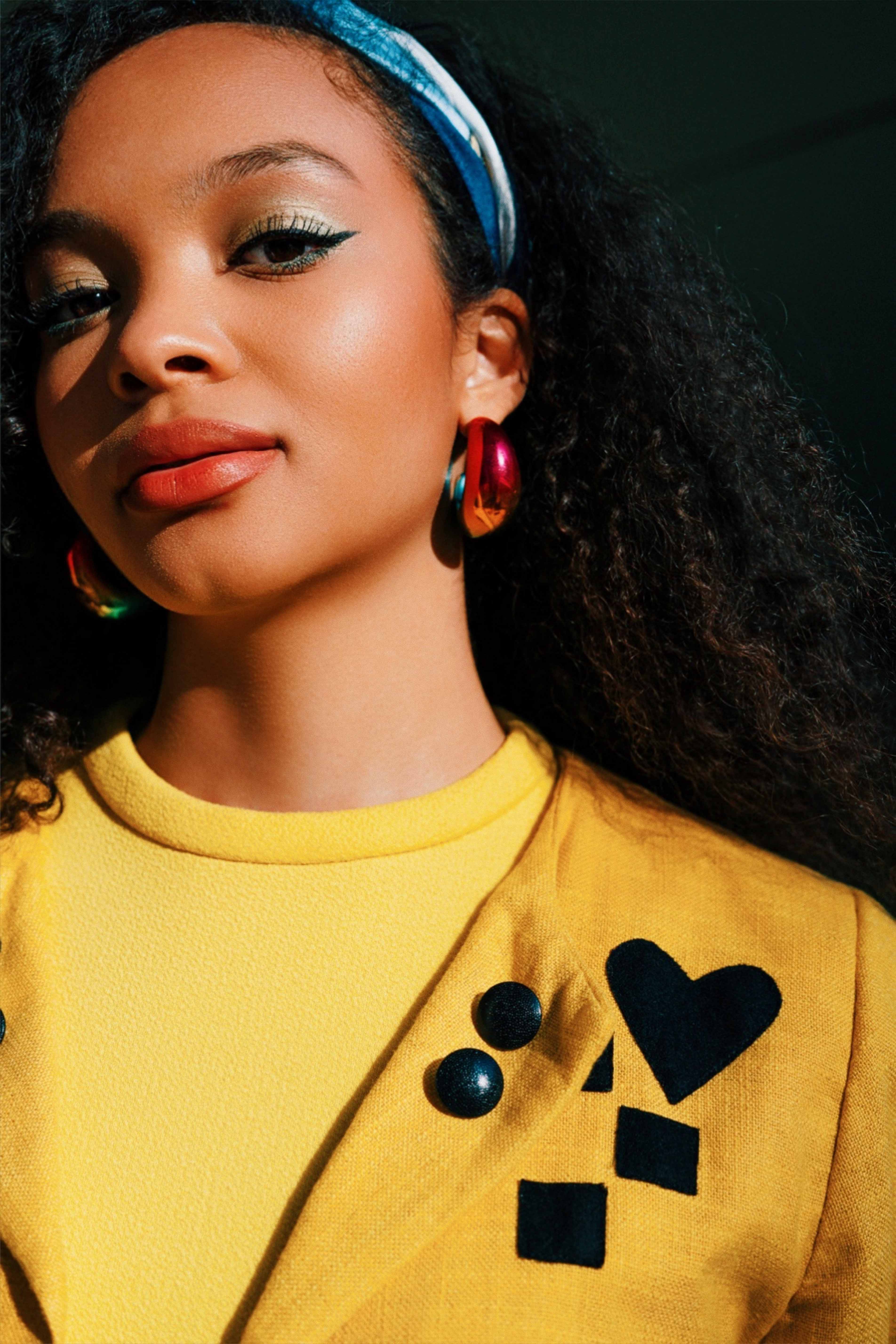 A model in a bright yellow blazer, wearing statement earrings and a blue headband. Shot by Alina Rudya on a Nikon Z6 III.