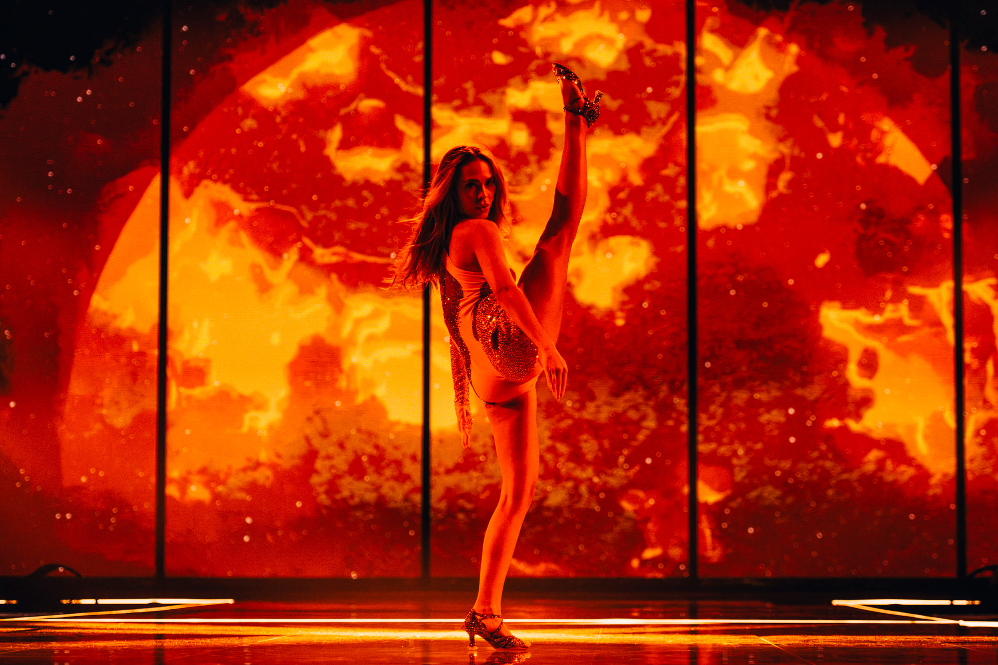 A performer on stage at Eurovision 2023, kicking one foot in the air, with bright orange lights behind them, shot by Sarah Louise Bennett with the Nikon Z7 II.

