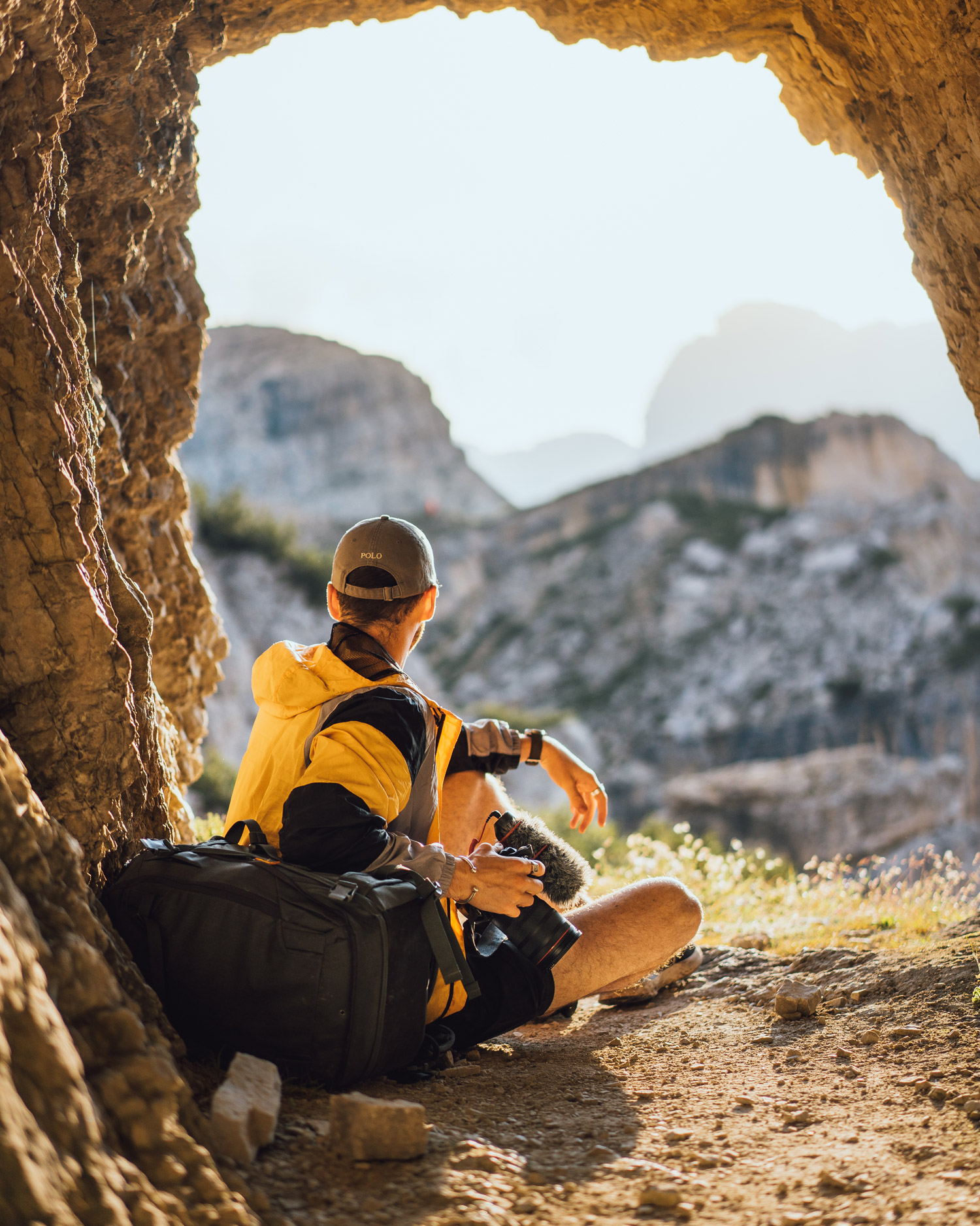 Jacob Murray blickt von einer Höhle aus auf einige Felsen, während er sich auf einige Taschen stützt und ein gelbes Oberteil trägt, aufgenommen mit der Sony A7 IV und dem Sony FE 55mm f/1.8 ZA.
