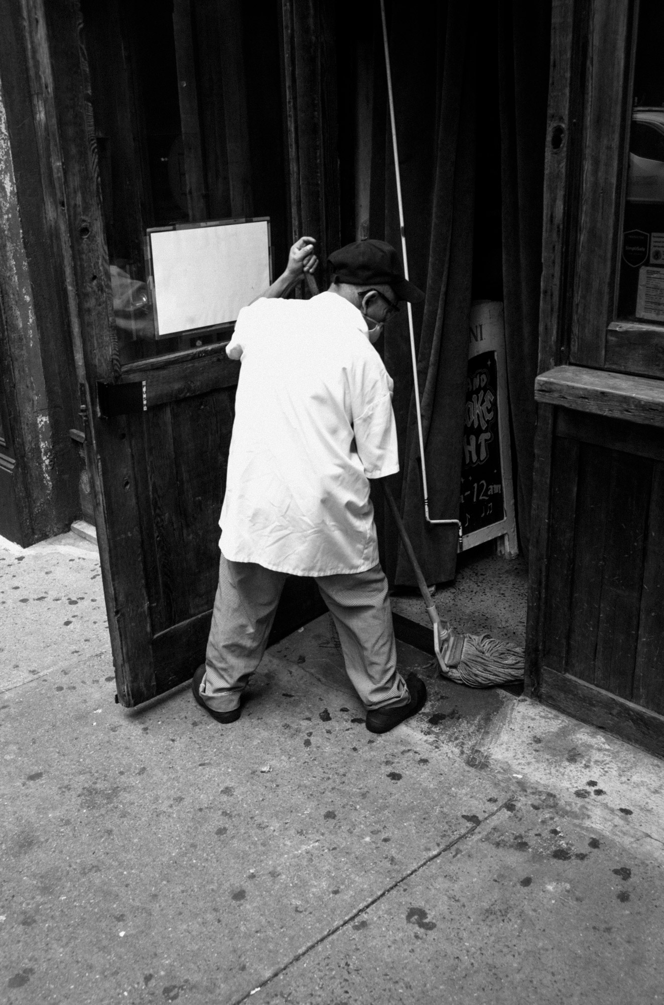 A black-and-white photo of a person sweeping the street