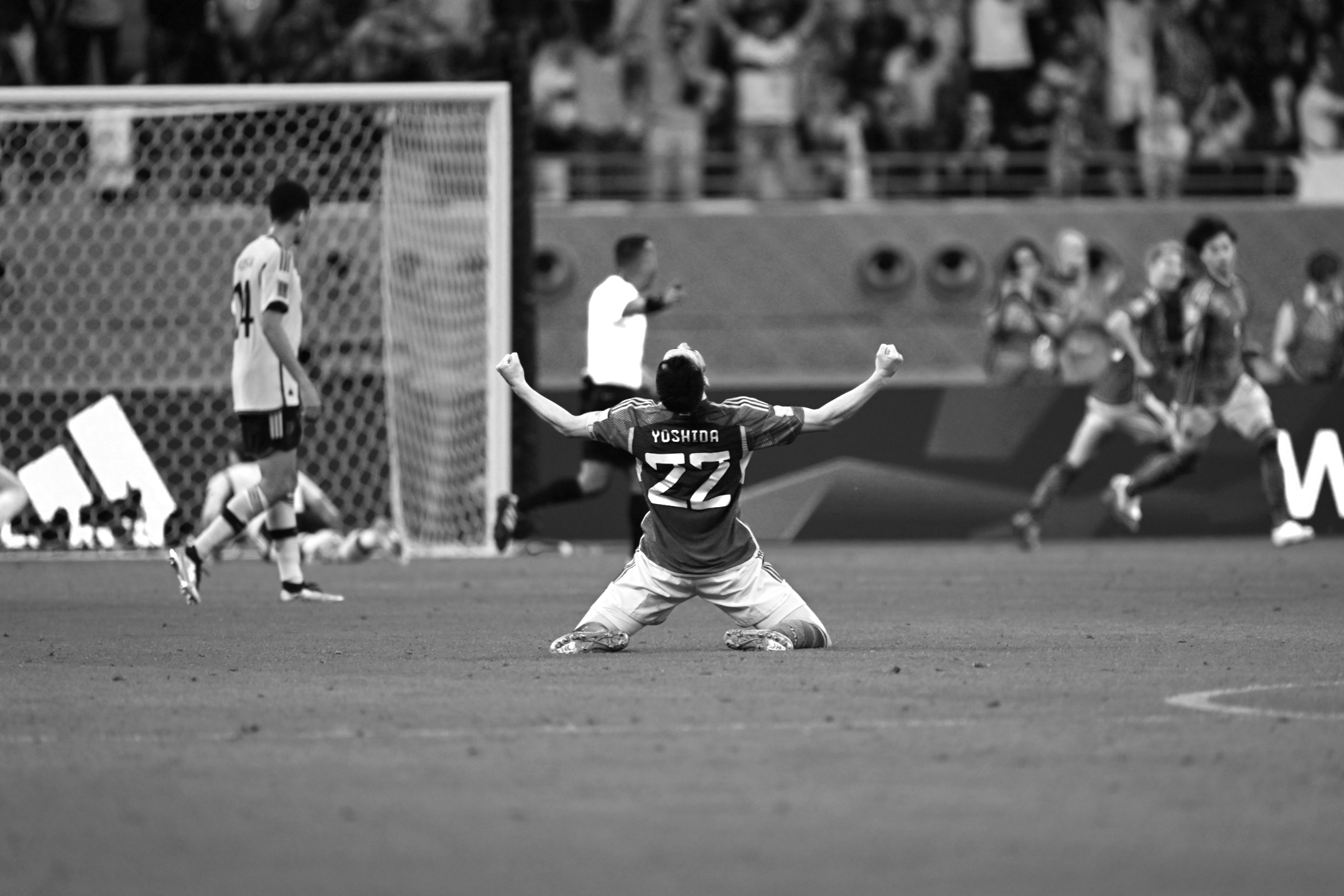 Ein Schwarz-Weiß-Foto des japanischen Nationalspielers Yoshida, der nach dem überraschenden 2:1-Sieg seiner Mannschaft gegen Deutschland bei der Weltmeisterschaft 2022 auf die Knie fällt und die Arme zum Jubeln hebt, aufgenommen von Ryu Voelkel mit einer Nikon Z9.