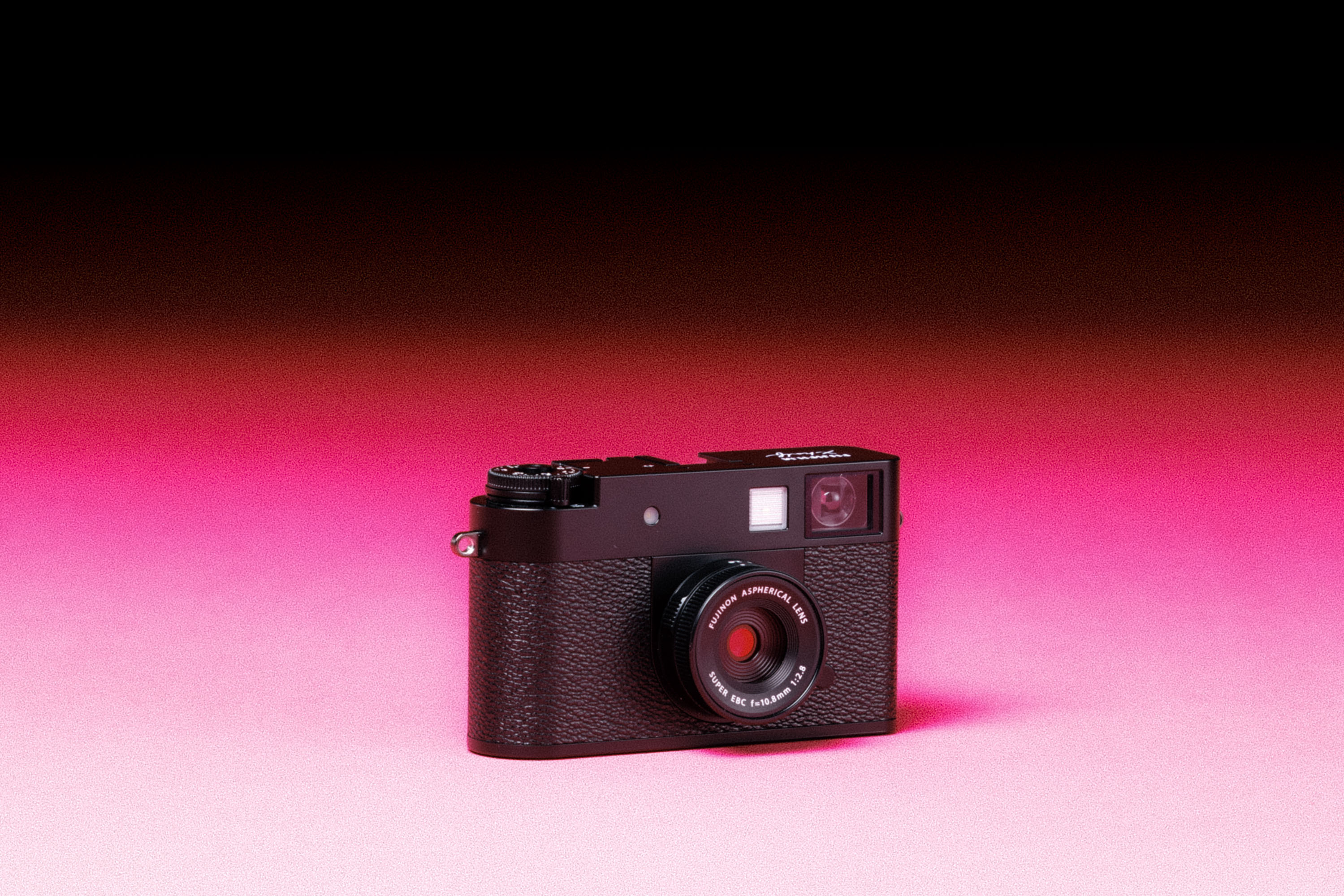 A used Fujifilm X Half camera with an added film-like grain effect on a graduated pink background.