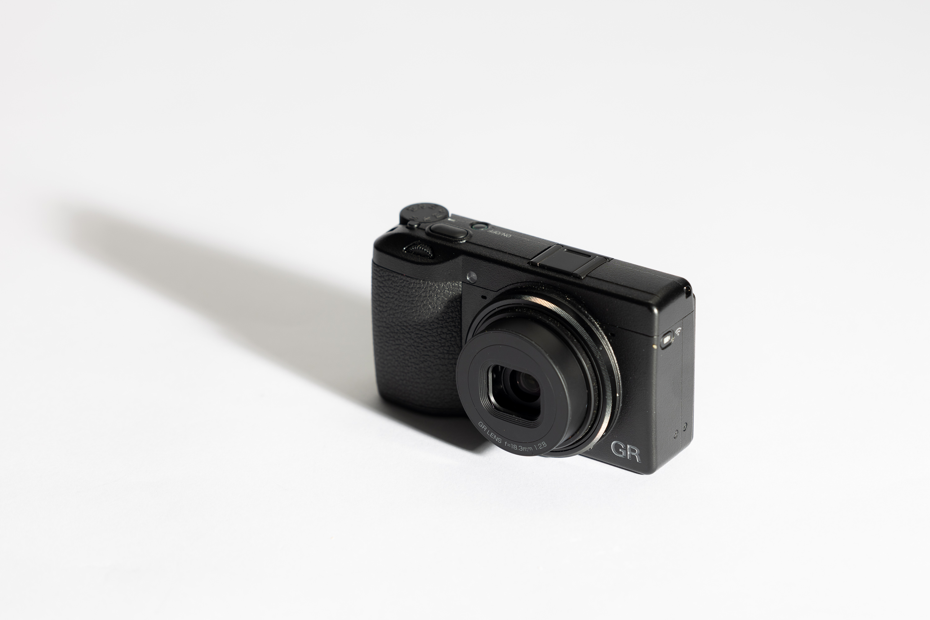 Vorderseite der Ricoh GR IV mit langem Schatten auf weißem Hintergrund