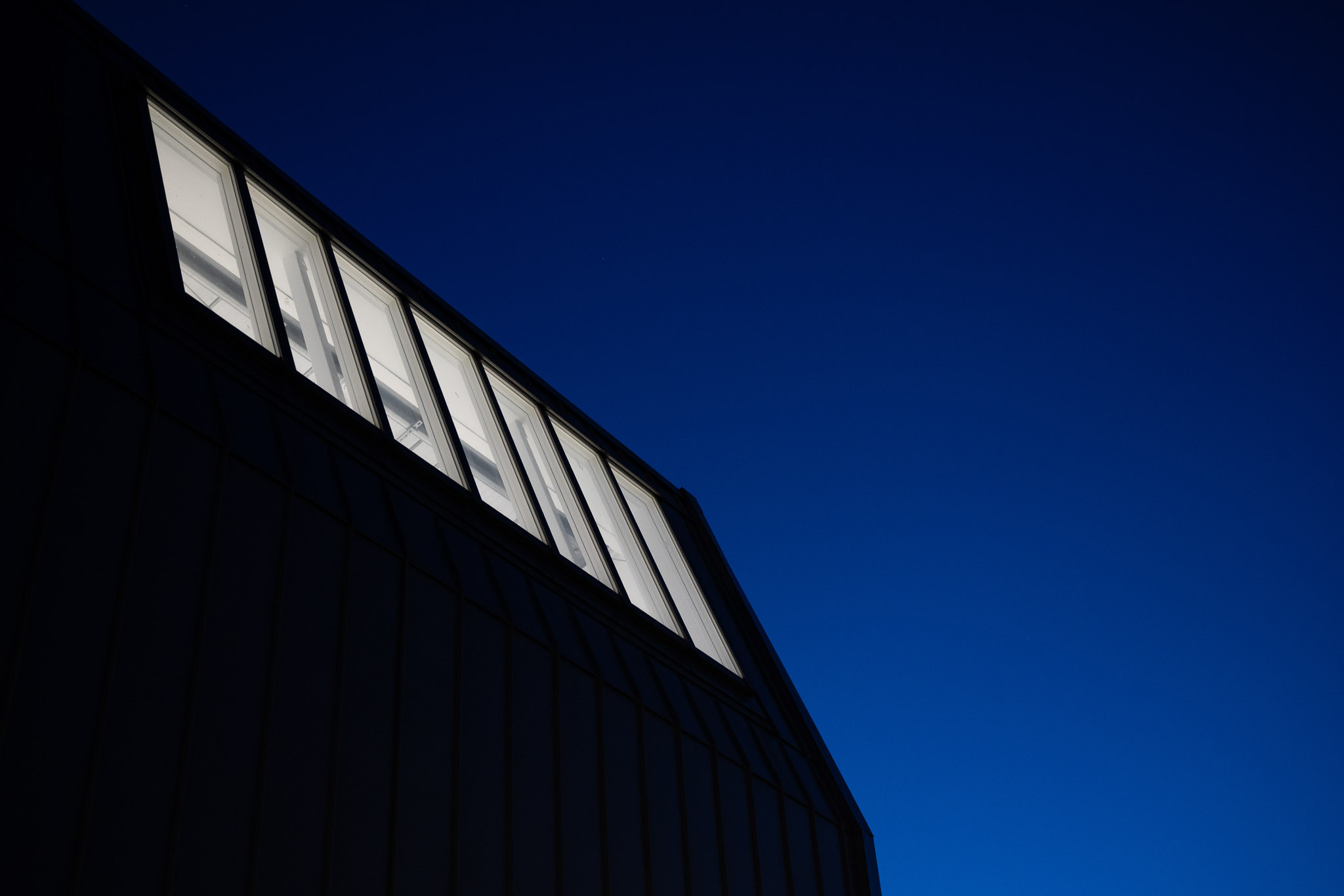 Modern building roofline with illuminated windows against a deep blue evening sky, photographed with the Nikon Zf by Amy Moore.