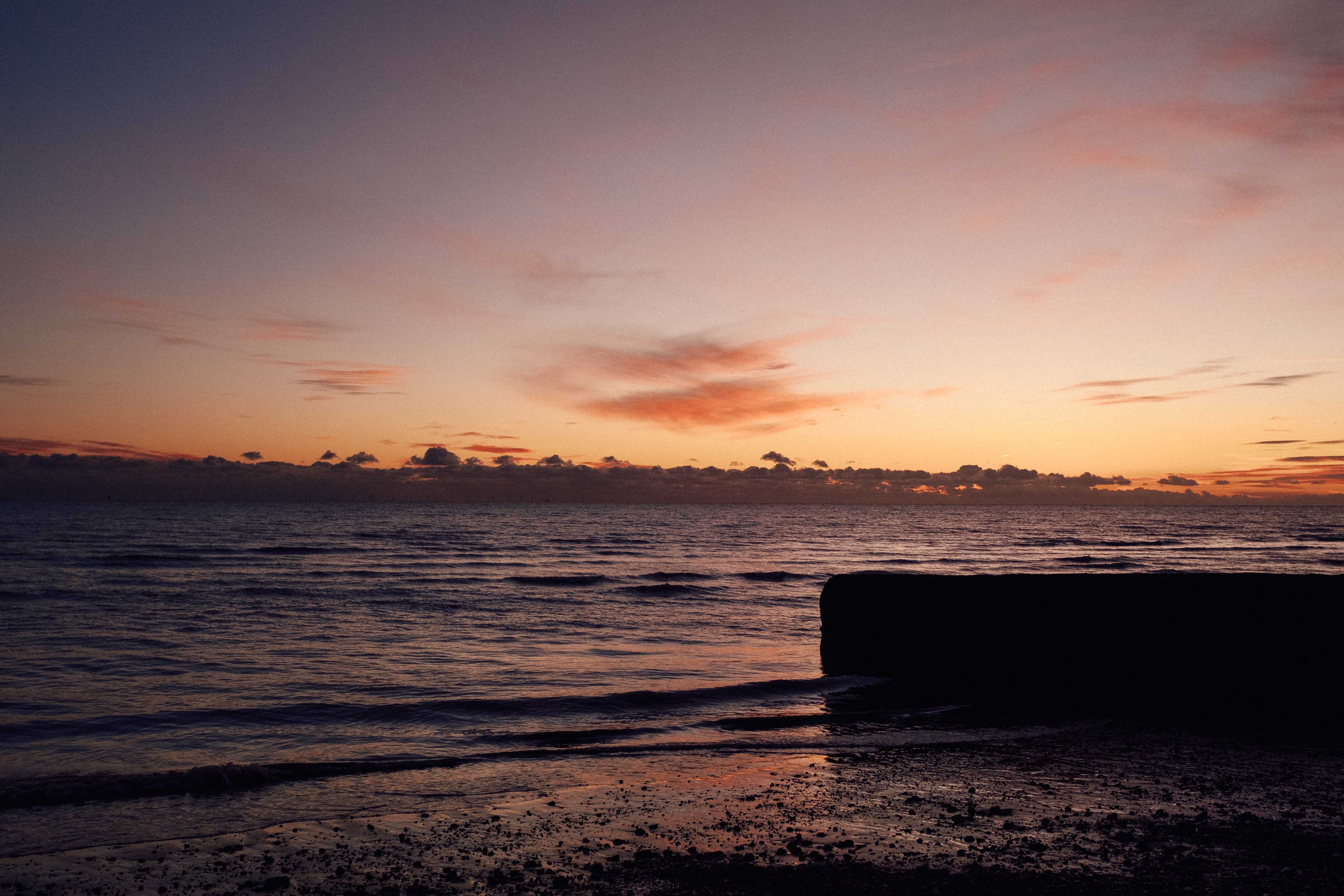 A beach and shorefront at sunset with a groyne in the bottom right. Taken by Connor Redmond on the Fujifilm X100F.