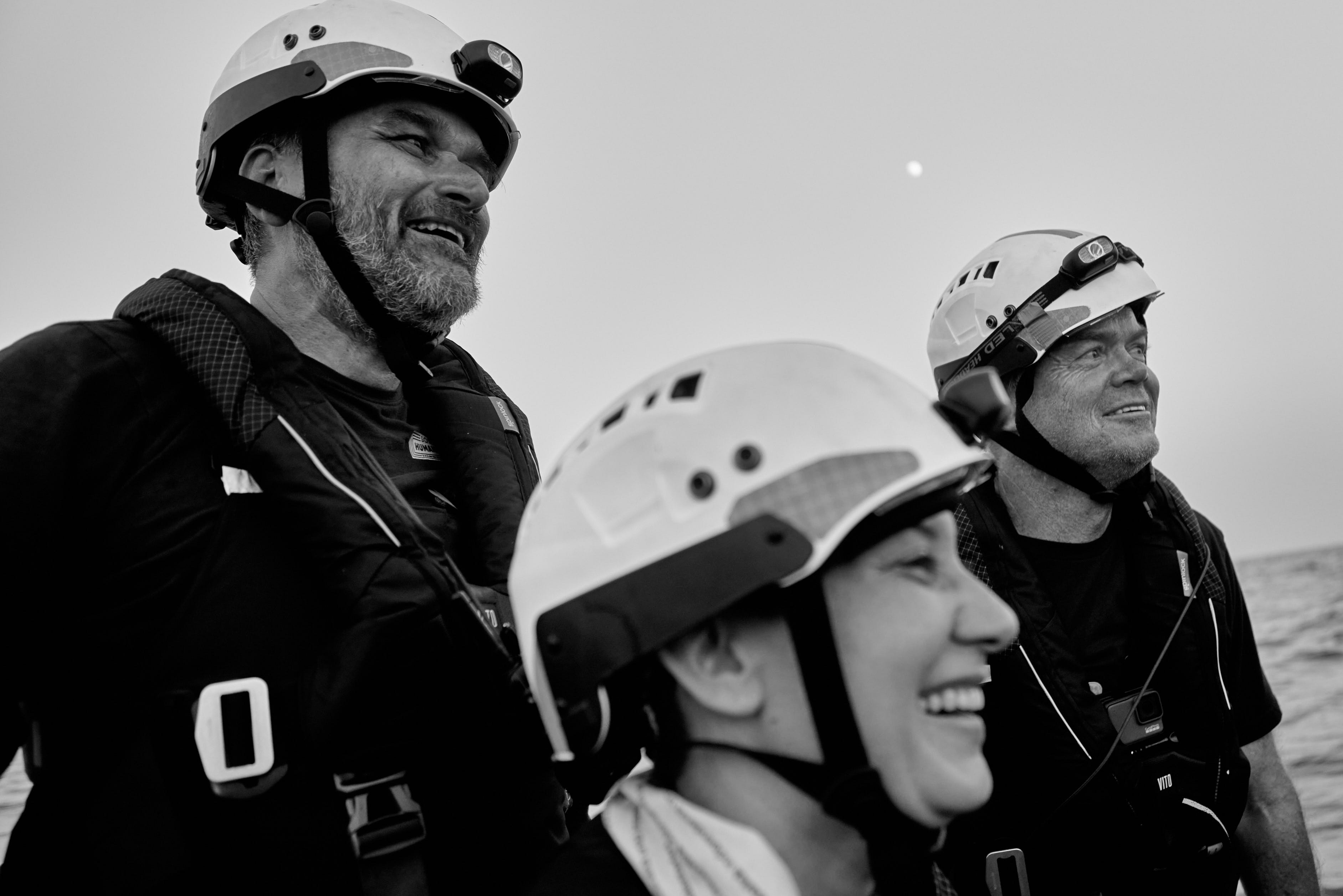 Photo en noir et blanc de trois membres de l'équipage du navire portant des casques, tous regardant dans la même direction et souriant.