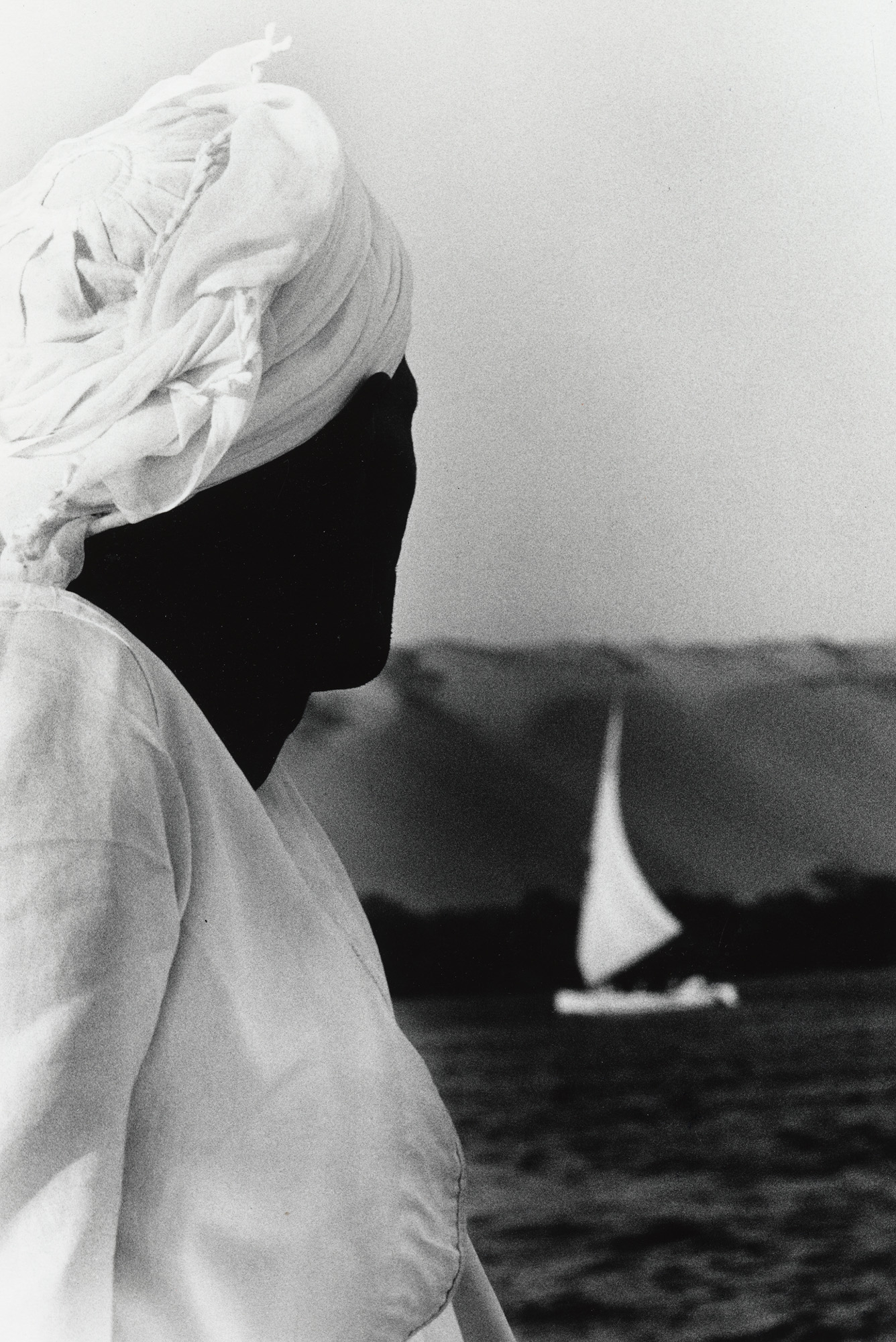 Ralph Gibson, imagen en blanco y negro de Leica de un hombre con turbante y ropa blanca junto al mar, mirando un velero.