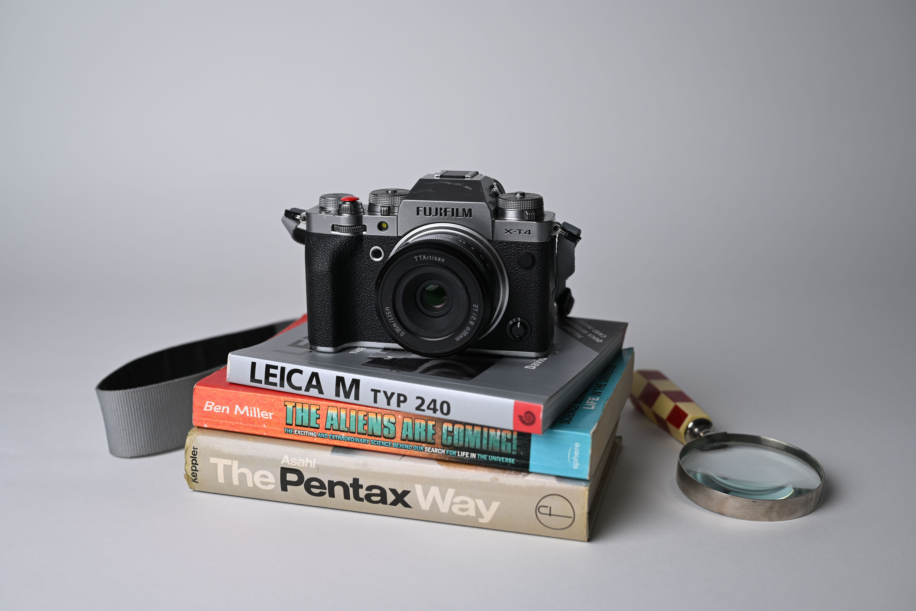 Fotovergleich zur Veranschaulichung der Körnungseinstellungen bei der Nikon Zf. Das Motiv ist die Fujifilm X-T4 auf einem Bücherstapel, wobei auf dem ersten Foto keine Körnung zu sehen ist und für das Vergleichsfoto die Körnungseinstellungen „Ein“, Korngröße „Groß“ und Kornstärke „4 von 6“ ausgewählt wurden.