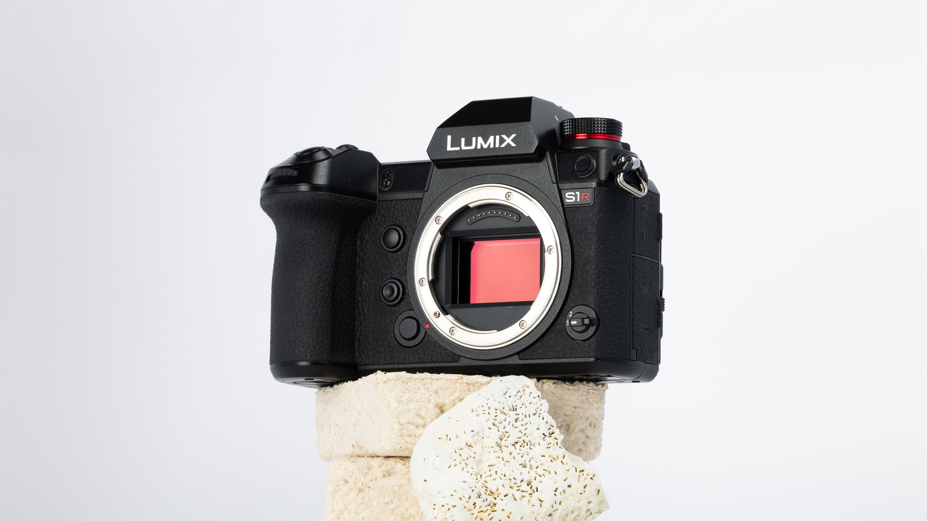 A product shot of a secondhand Panasonic S1R camera propped up on a rocky podium on an off white background.