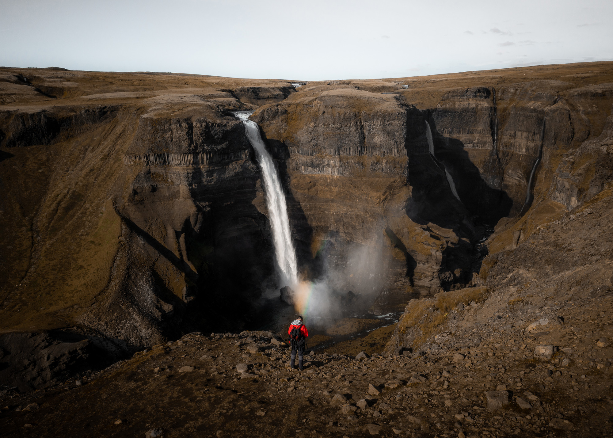An aerial drone photo of a figure in a red coat standing on the edge of a cliff with a waterfall in the background in Iceland, shot by Paul Watson DJI Mavic 2 Pro
