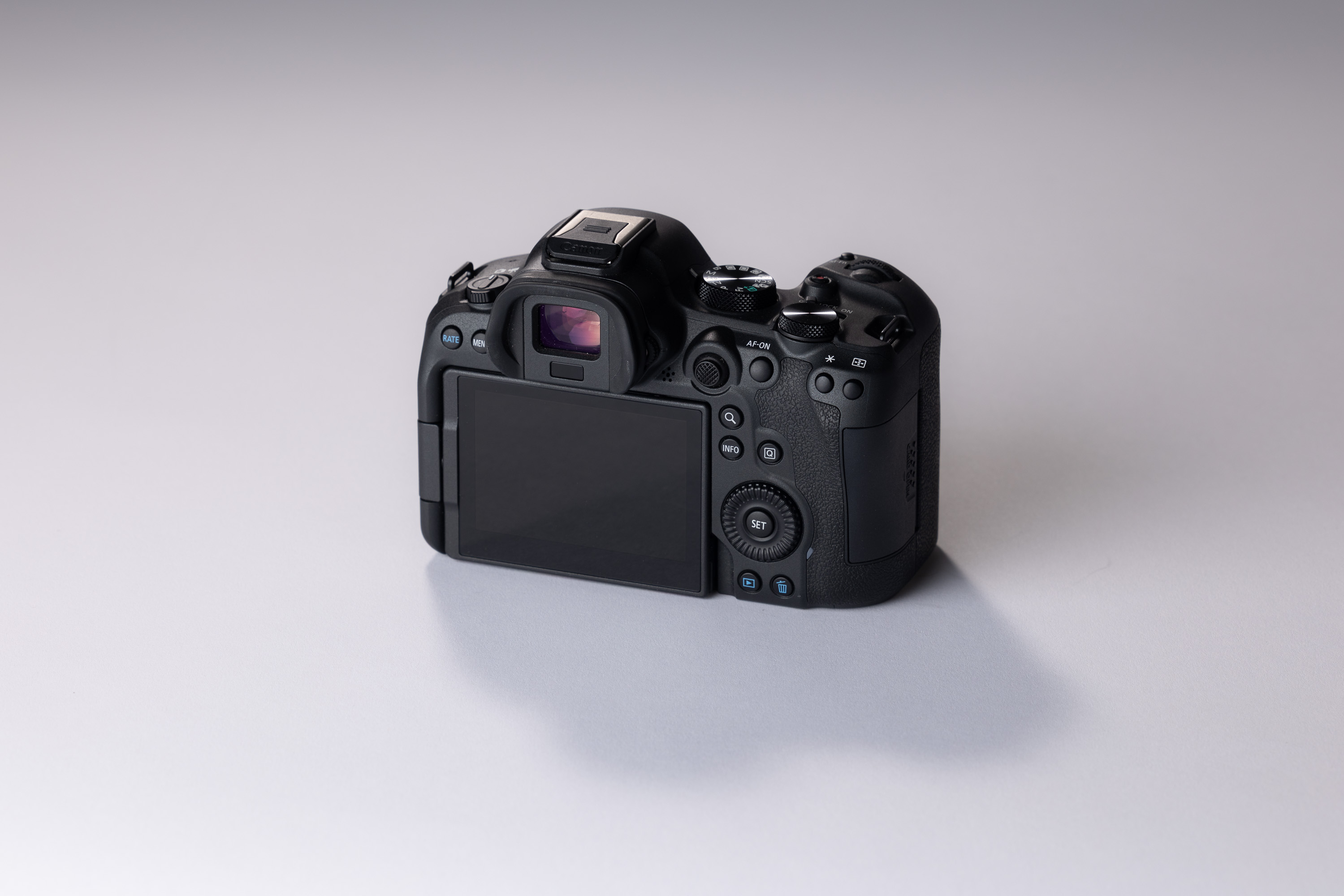 The back of a used Canon EO6 Mark II showing its viewfinder, screen and dials. The camera sits on a white background, with a shadow stretching out in front of it