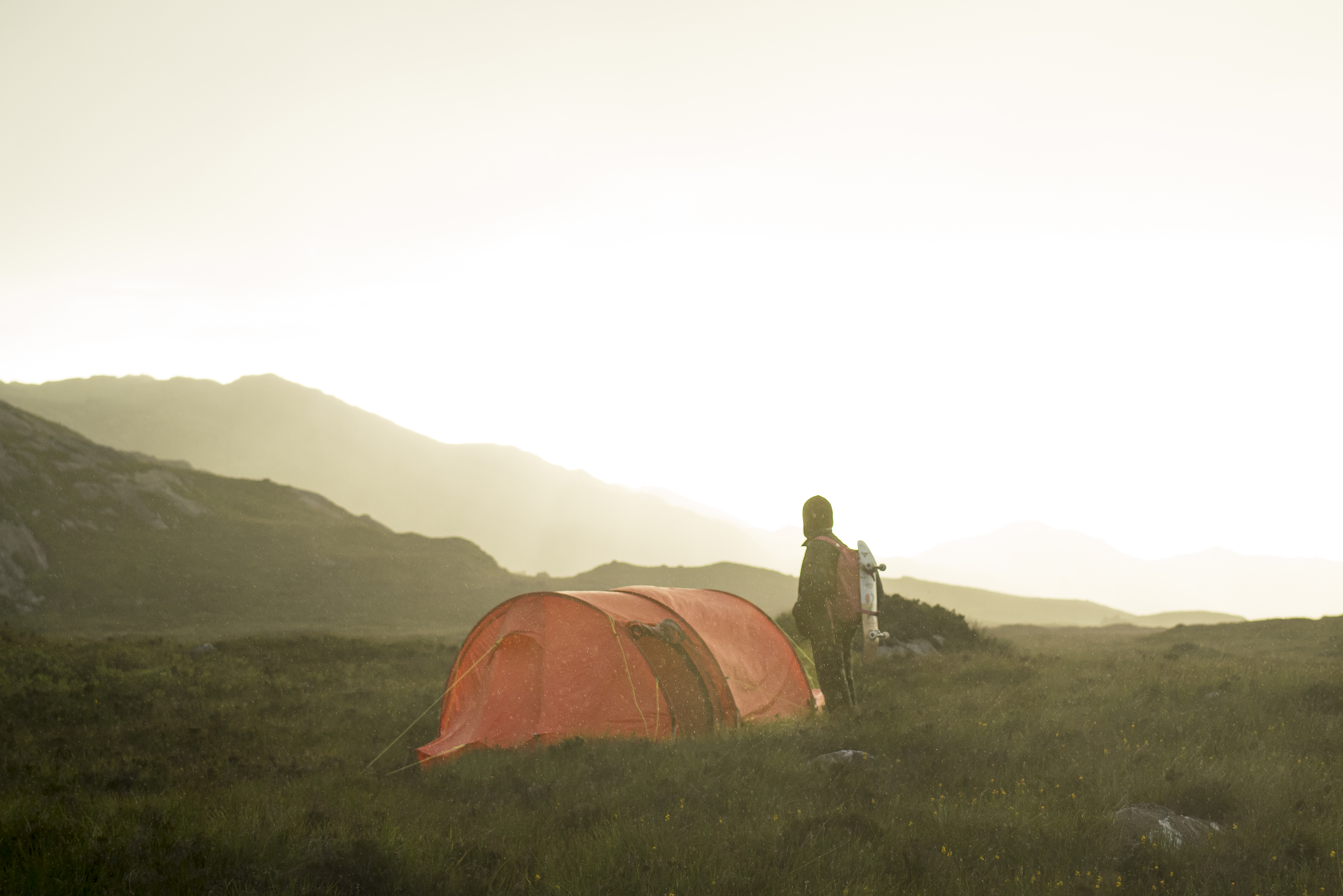 A skateboarder setting up an orange tent in the Scottish Highlands