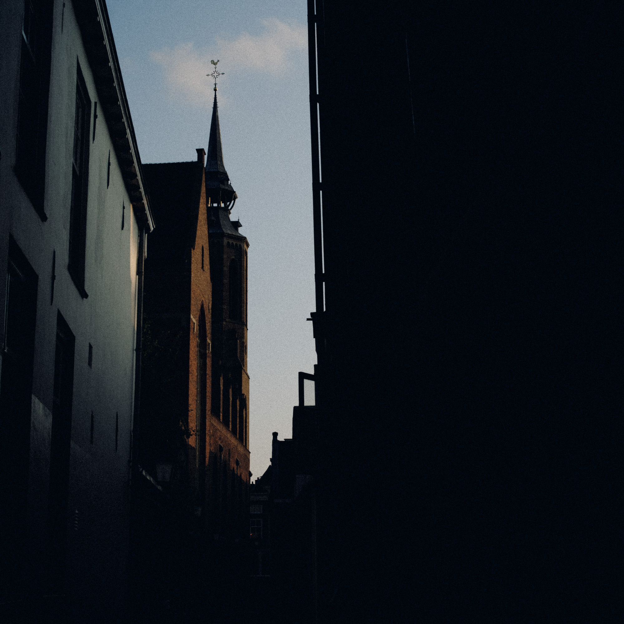 Sample photo showing a tall church spire and historic buildings rise dramatically between narrow, dark alley walls under a twilight sky.