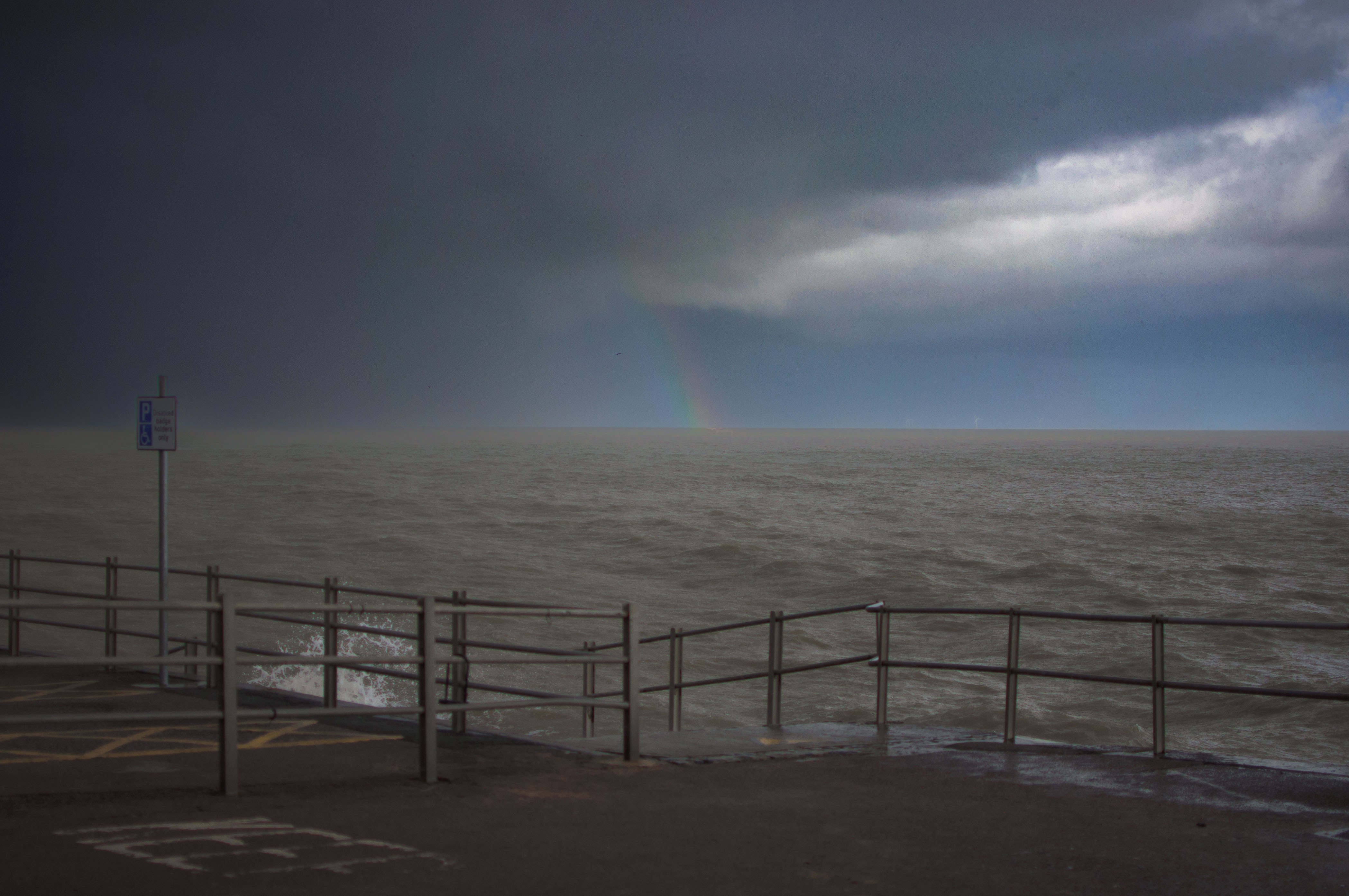 Ein schwacher Regenbogen taucht bei stürmischem Wetter aus dem Meer auf. Von Connor Redmond.

