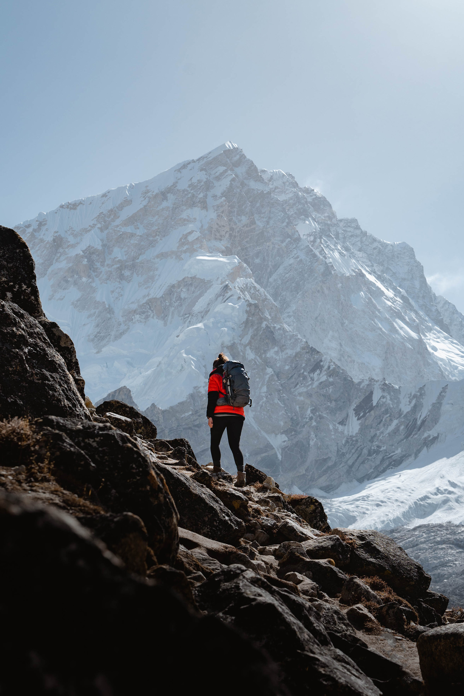 A hiker in red wearing a backpack clambers over boulders towards a vast snow-topped mountain, shot by Jack Anstey with the Sony A7 IV and Sony FE 24-70mm f/2.8 GM