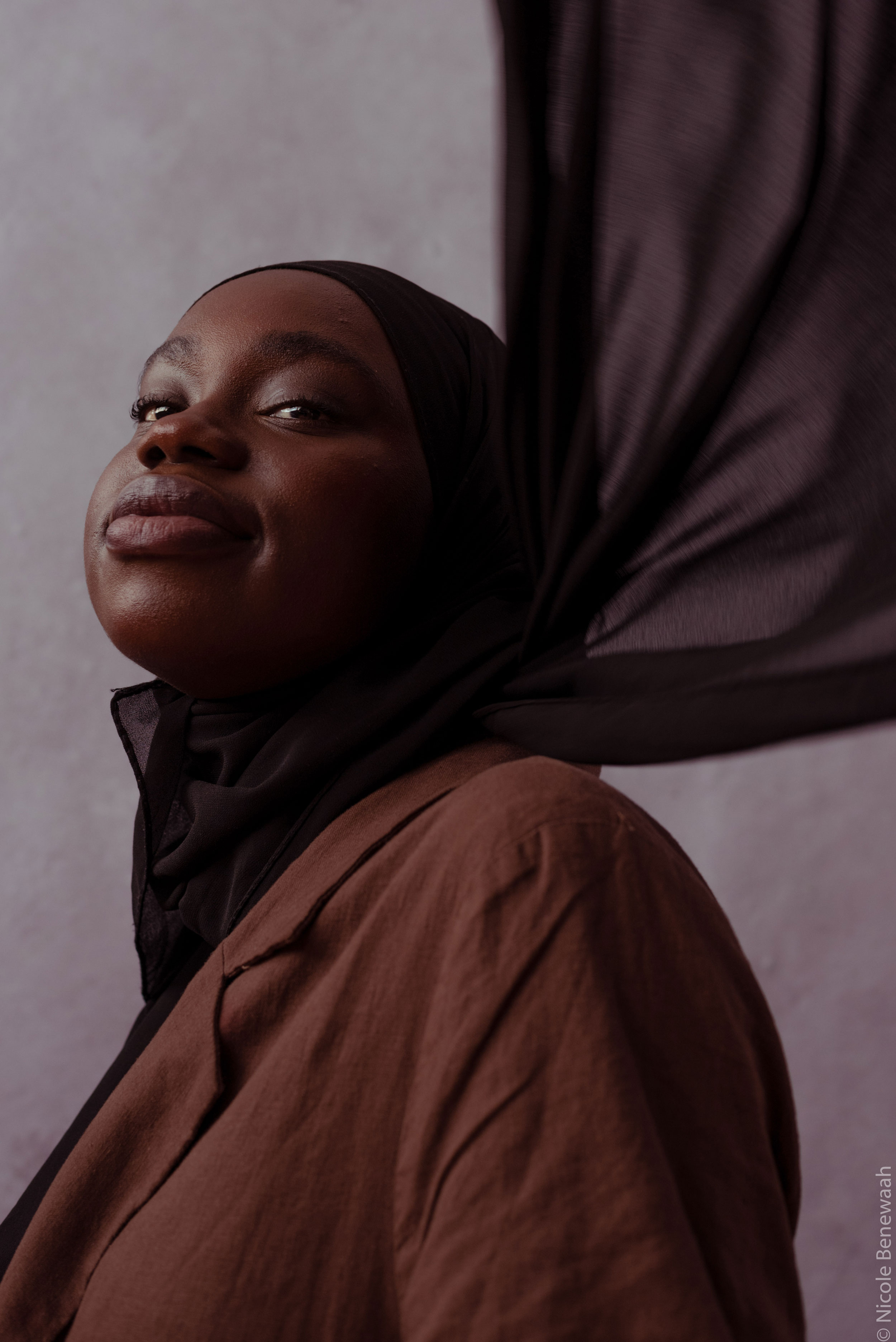 Portrait of a Black woman with headscarf blowing backwards, shot by Nicole Benewaah