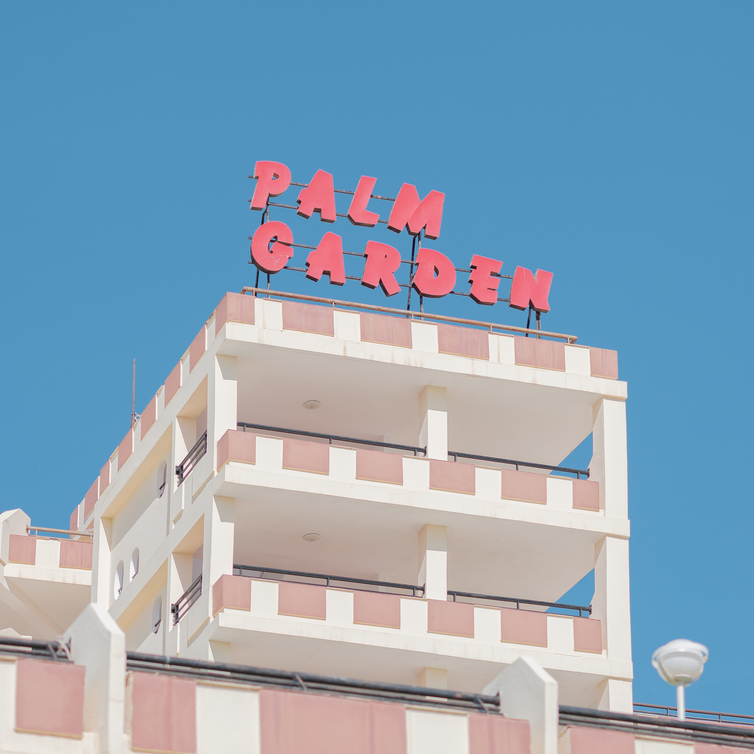 A big hotel with a sign that reads ‘Palm Garden’ on it in a pale pink colour.  Taken on the Fujifilm GFX 50R by Connor Redmond. 
