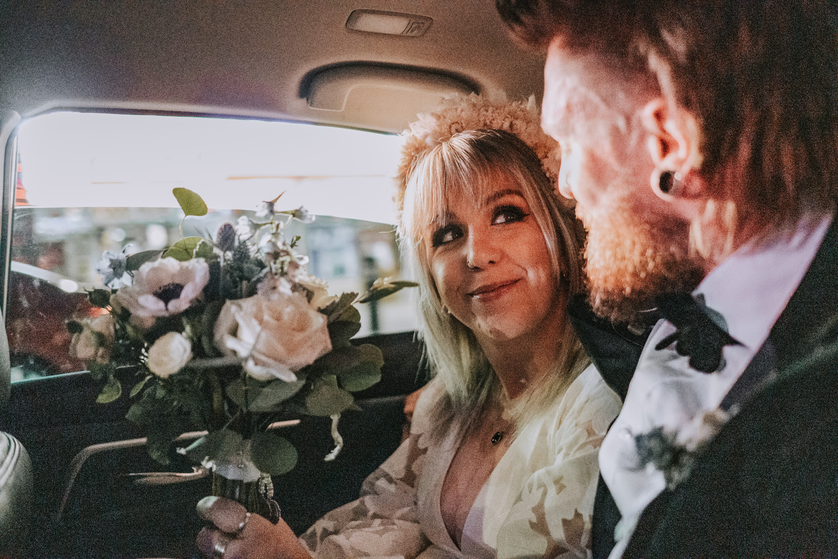 Gros plan d'une mariée et d'un marié qui se regardent en tenant un bouquet de fleurs à l'arrière d'une voiture. Photo prise par Matthew Palmer avec un Fujifilm X-T4