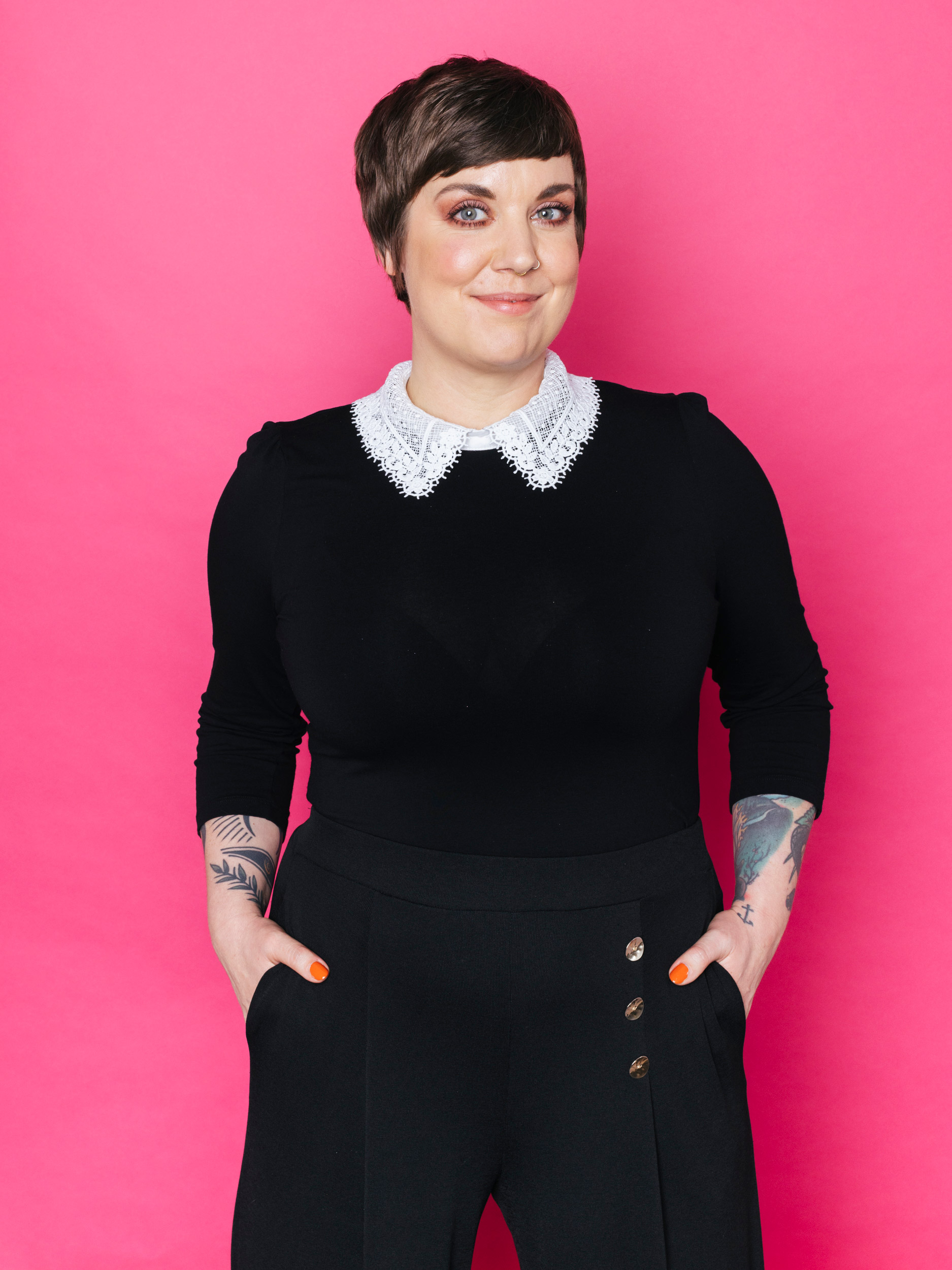 
Amerikanische Einstellung einer Person in schwarzer Kleidung mit den Händen in den Taschen vor einem pinken Hintergrund.

