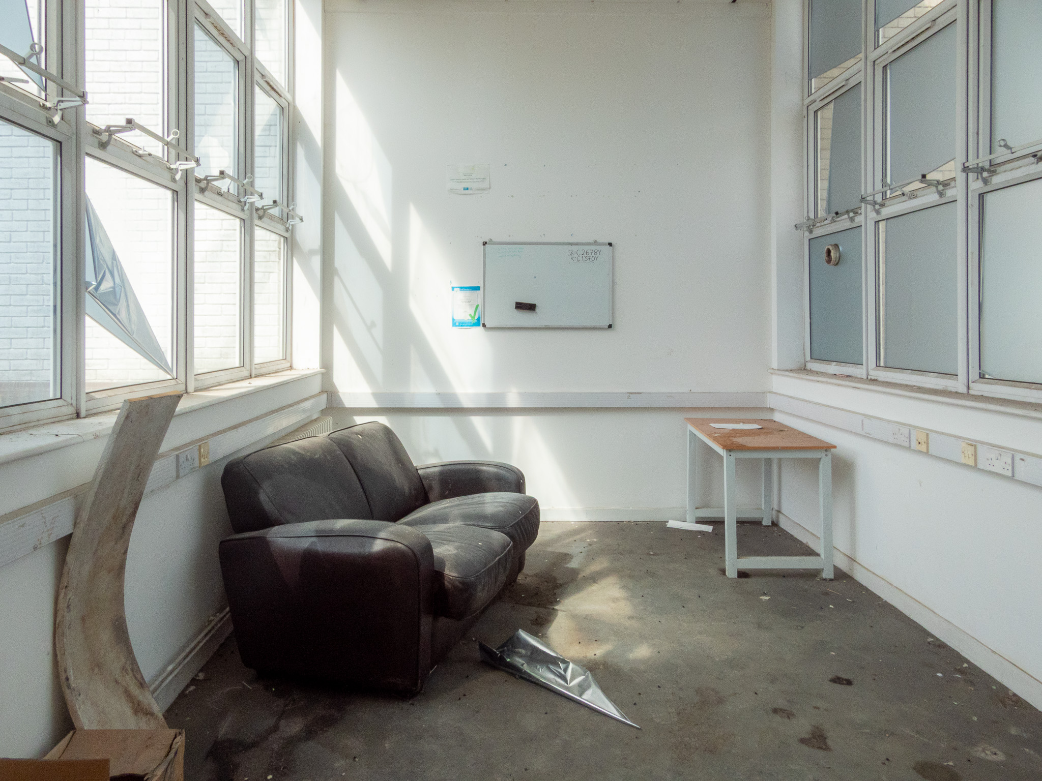 A wide shot of an abandoned office room with a dusty sofa on the left.