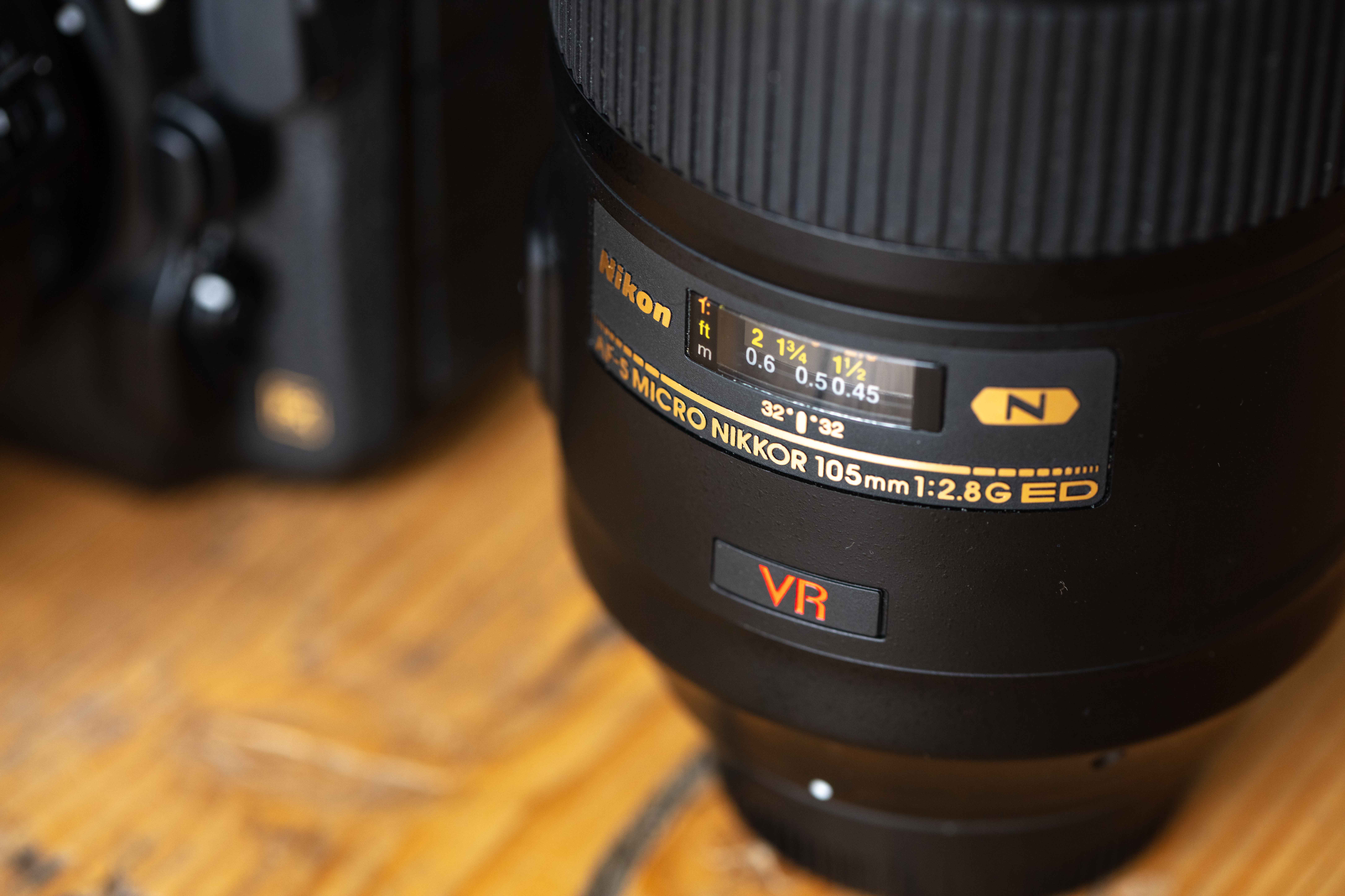 Close-up shot of a Nikon AF-S Micro NIKKOR 105mm f/2.8G ED lens on a wooden surface.