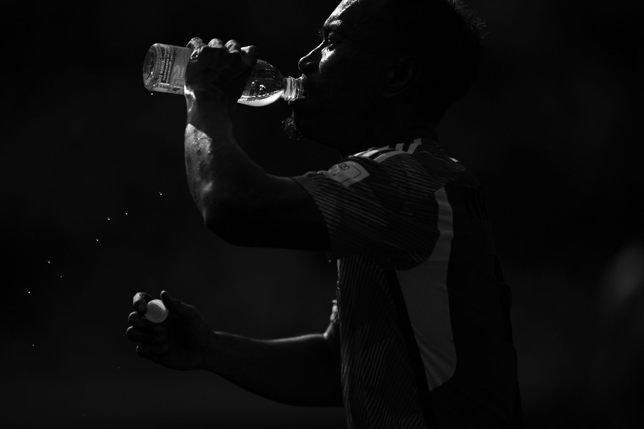 Ein Schwarz-Weiß-Foto eines Fußballspielers, der während der 1:0-Niederlage Japans gegen Costa Rica bei der Fußball-Weltmeisterschaft 2022 aus einer Wasserflasche trinkt, aufgenommen von Ryu Voelkel mit einer Nikon Z9.