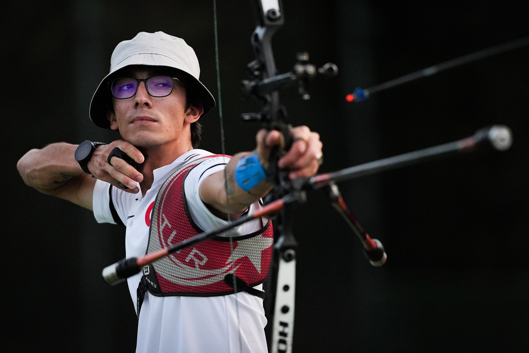 An archer in a white and red uniform loosens an arrow which is captured mid-flight.