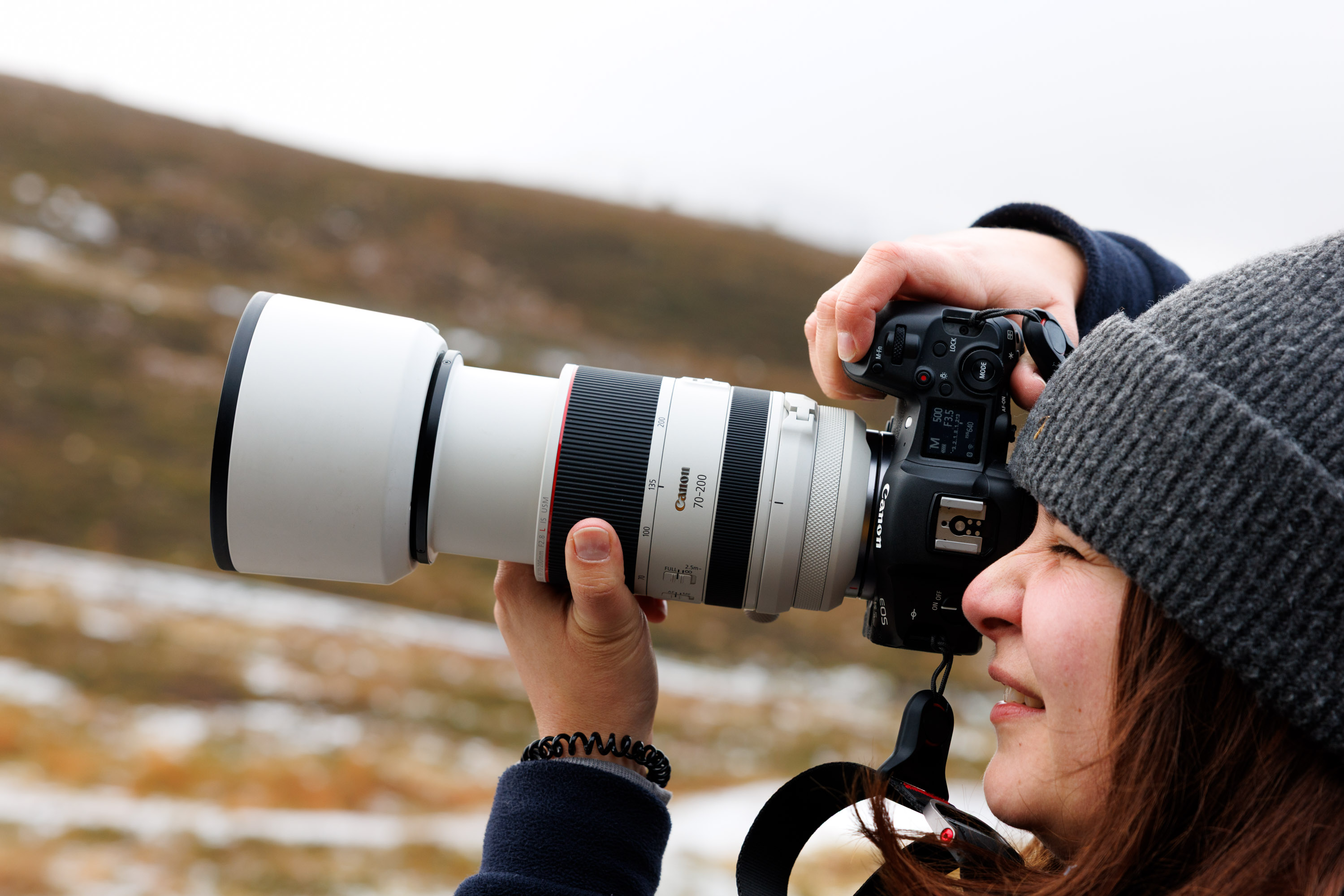 A photographer using a Canon telephoto lens with a lens hood during snowy conditions.