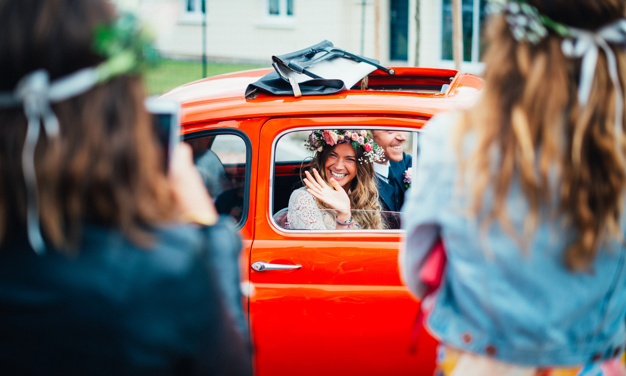 A bride greets her guests from the window of her red car. Photo taken by Gauthier Le Guen with a Canon R6.
