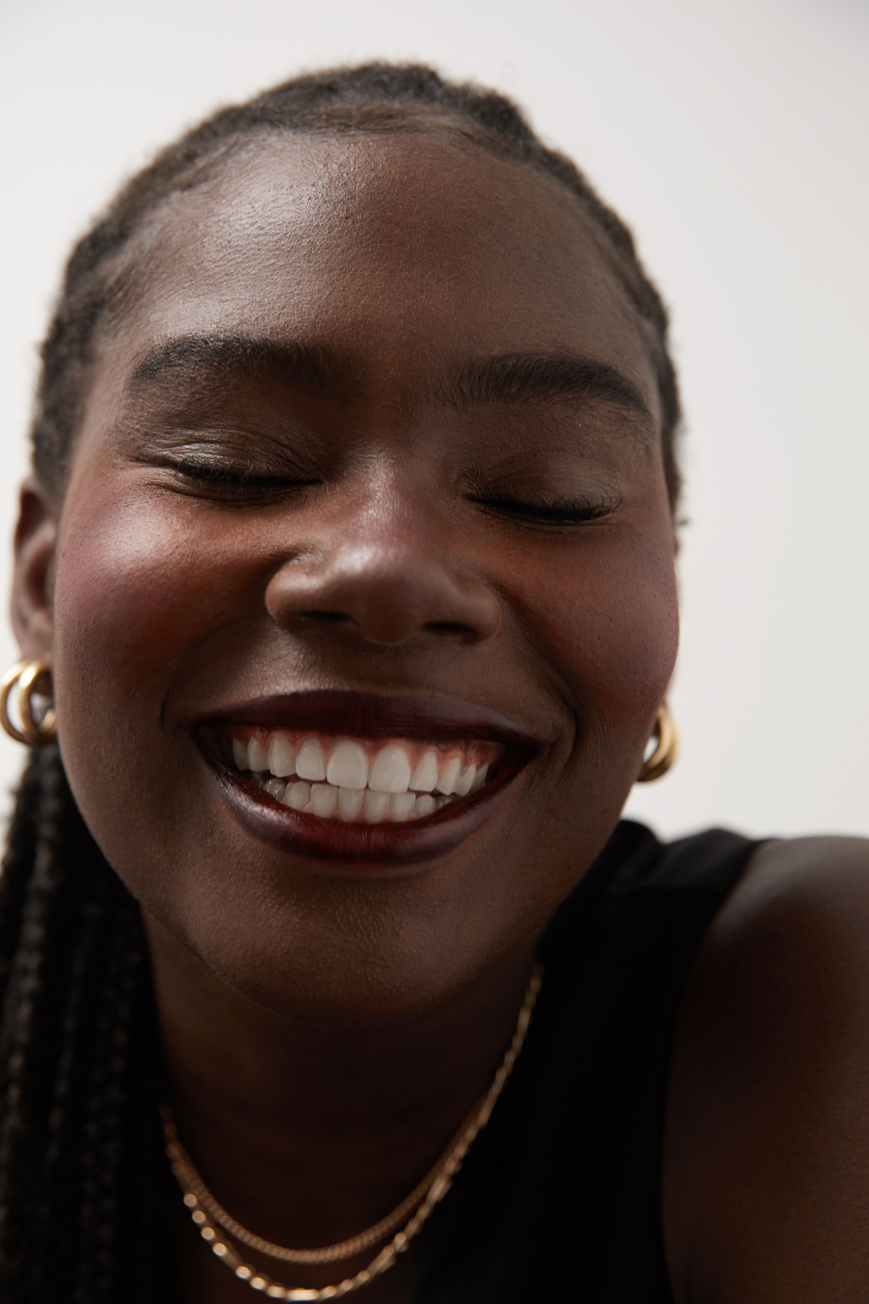 Close-up of a Black woman with a beaming smile and closed eyes, shot by Samia Rachel
