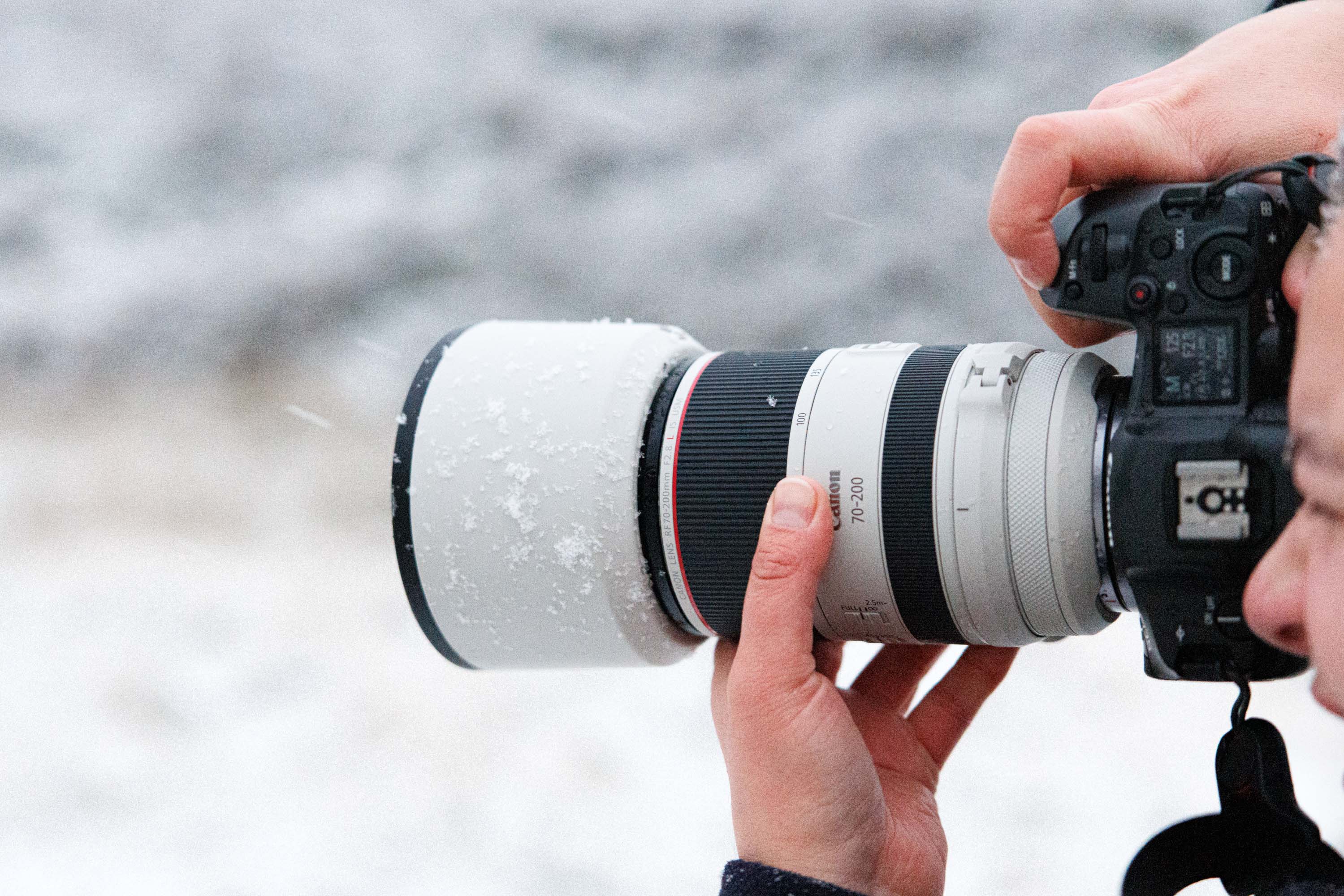 Close-up of a photographer using a Canon telephoto lens with a lens hood during snowy conditions.