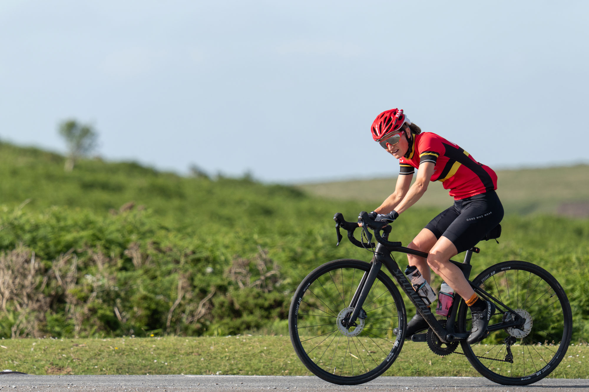 A cyclist in red cycling on a road in Dartmoor National Park. Behind them is green shrubbery, out of focus. Photo by Amy Moore with the Panasonic S1R II. 