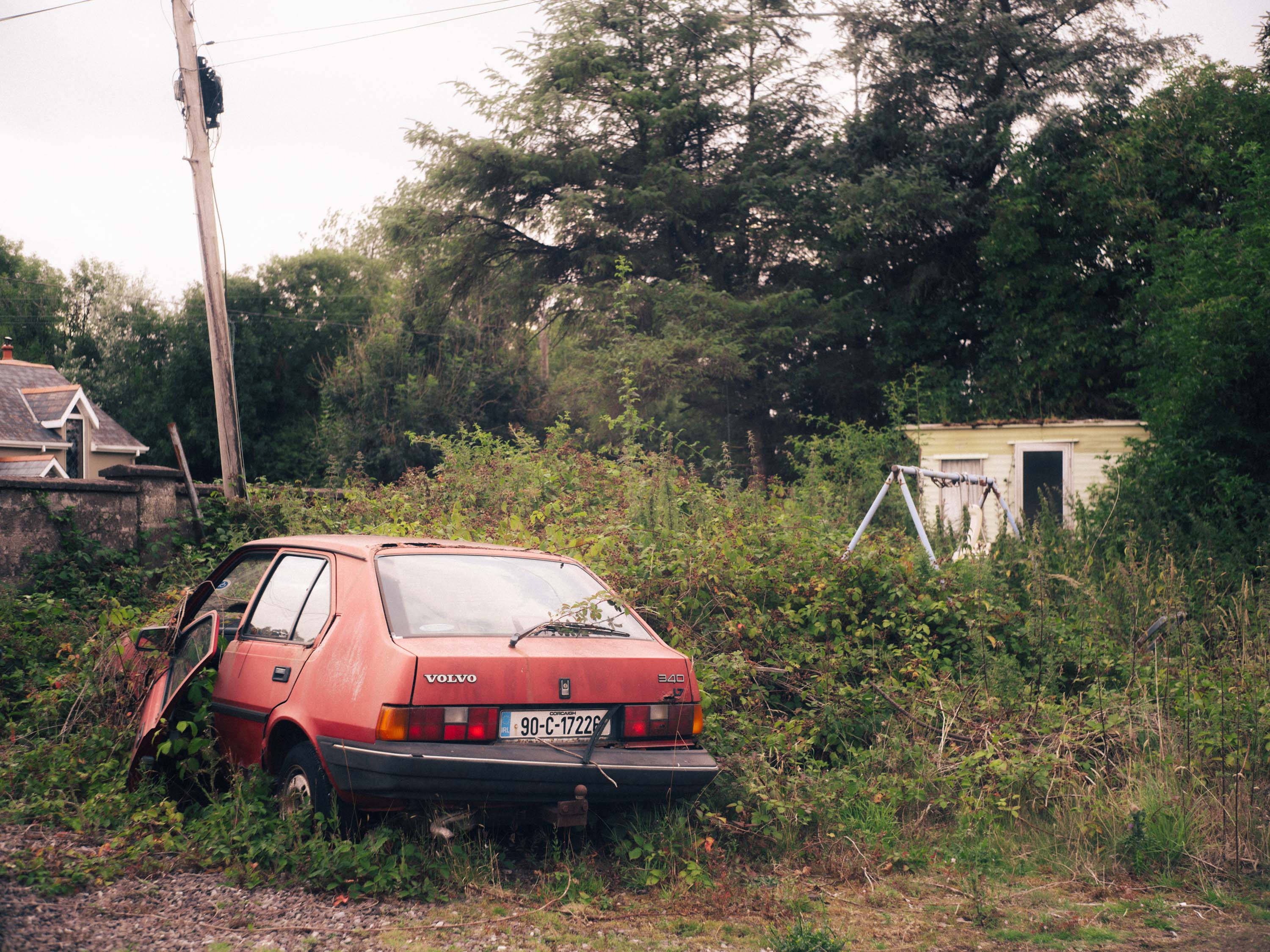 A rundown abandoned red car is being taken over by grass and nature. Taken on the Fujifilm GFX 50R by Ian Howorth. 

