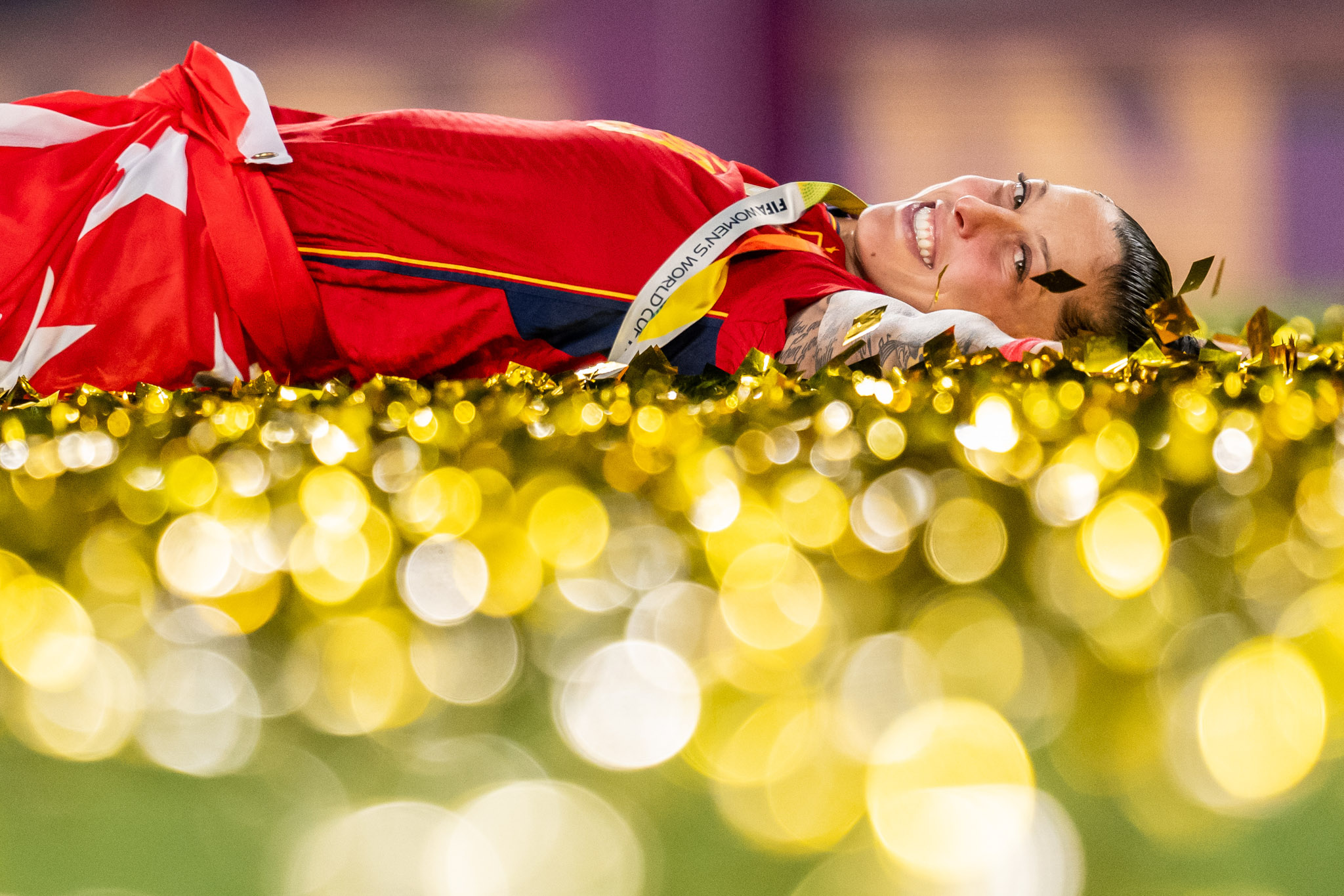 A low-angle shot on the ground of a Spanish football player with the foreground covered in golden celebration confetti. By Mathias Bergeld.