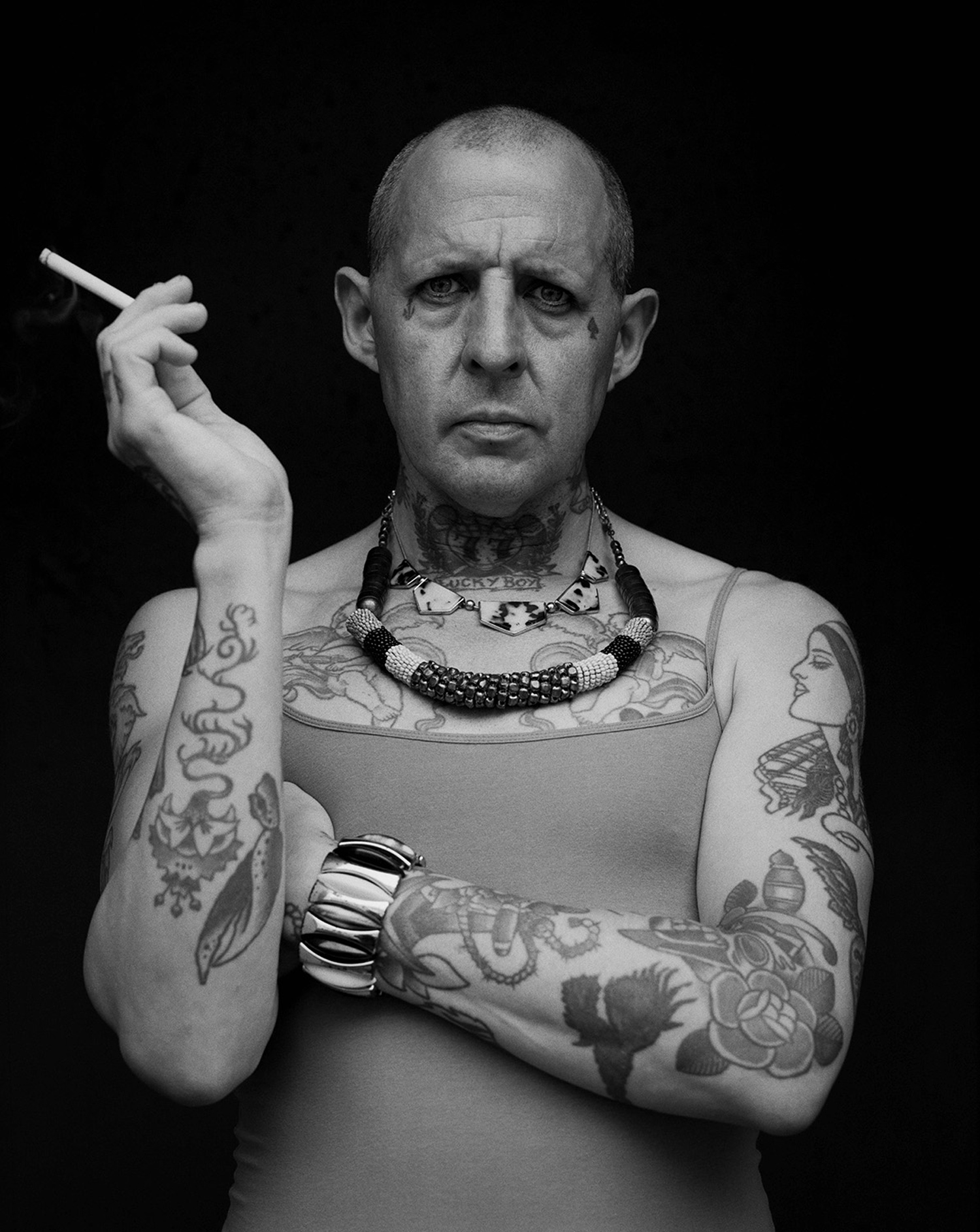 Une personne fortement tatouée avec une cigarette et des bijoux imposants.