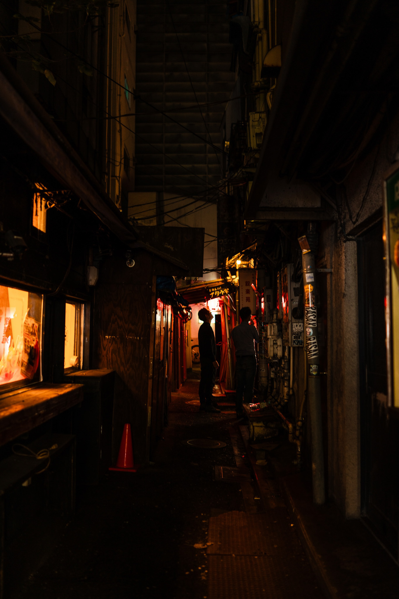 A narrow urban alleyway in Japan, illuminated by warm ambient light from nearby shops, capturing the essence of nightlife and authentic local culture. Photographed by Ruby Cruden with a Sony DSC-RX1 RM II.