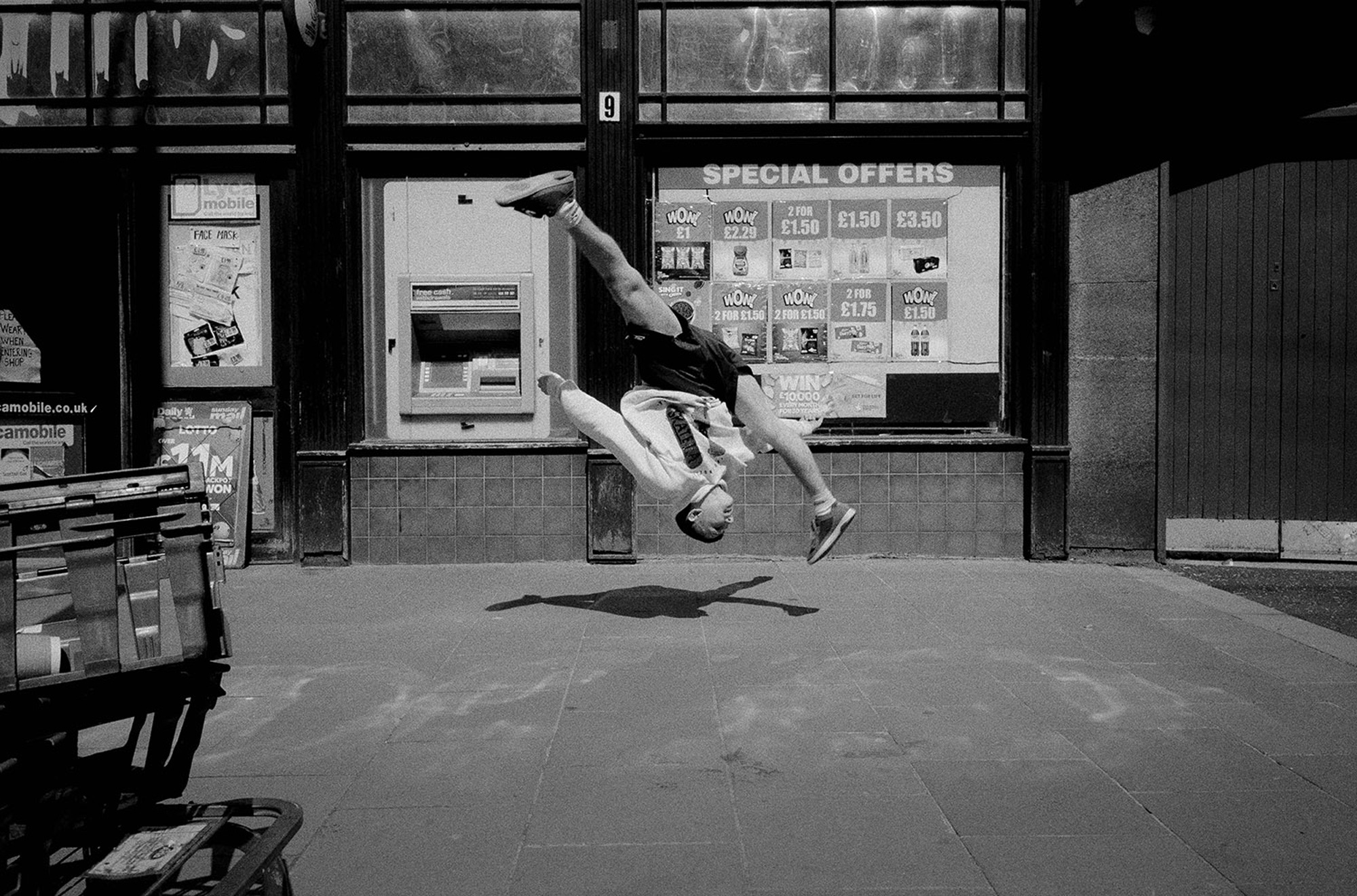 Een zwart-witfoto van Josh die een backflip uitvoert buiten een winkel, gefotografeerd door Simon Murphy