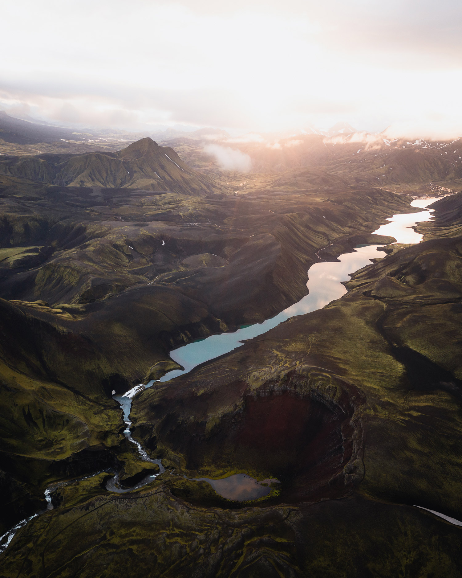An aerial drone landscape photo of a river running into a lake in Iceland, there are grass-covered hills and mountains in the background, shot by Paul Watson with a DJI Mavic 2 Pro