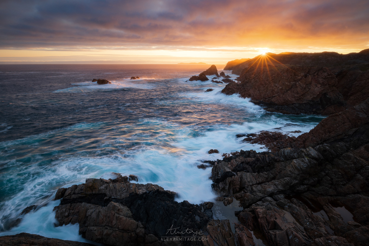 Waves crash against the seaside as the sun sets at dusk.